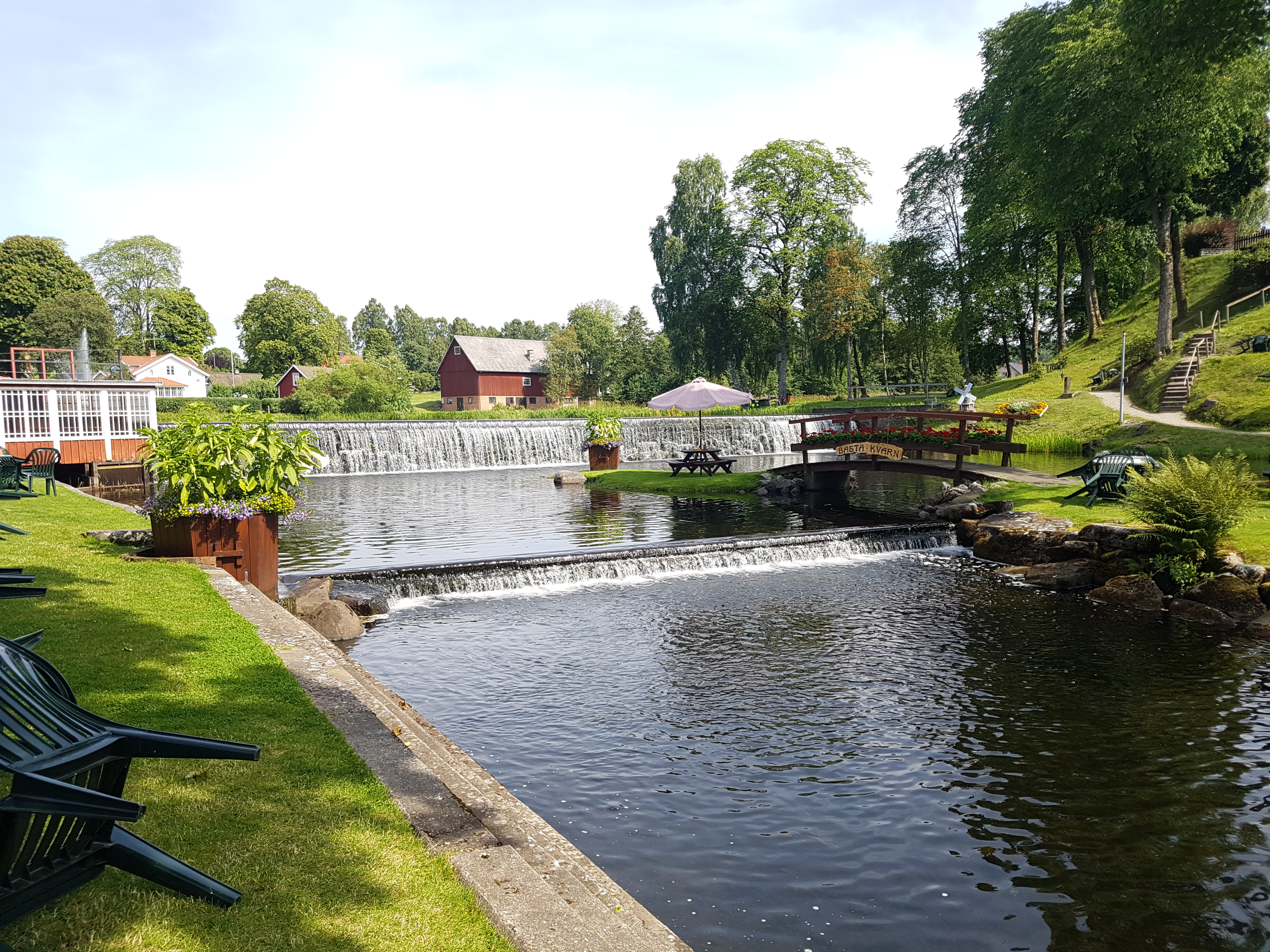 Litet vattenfall och grönytor och ett litet hus med glasveranda.
