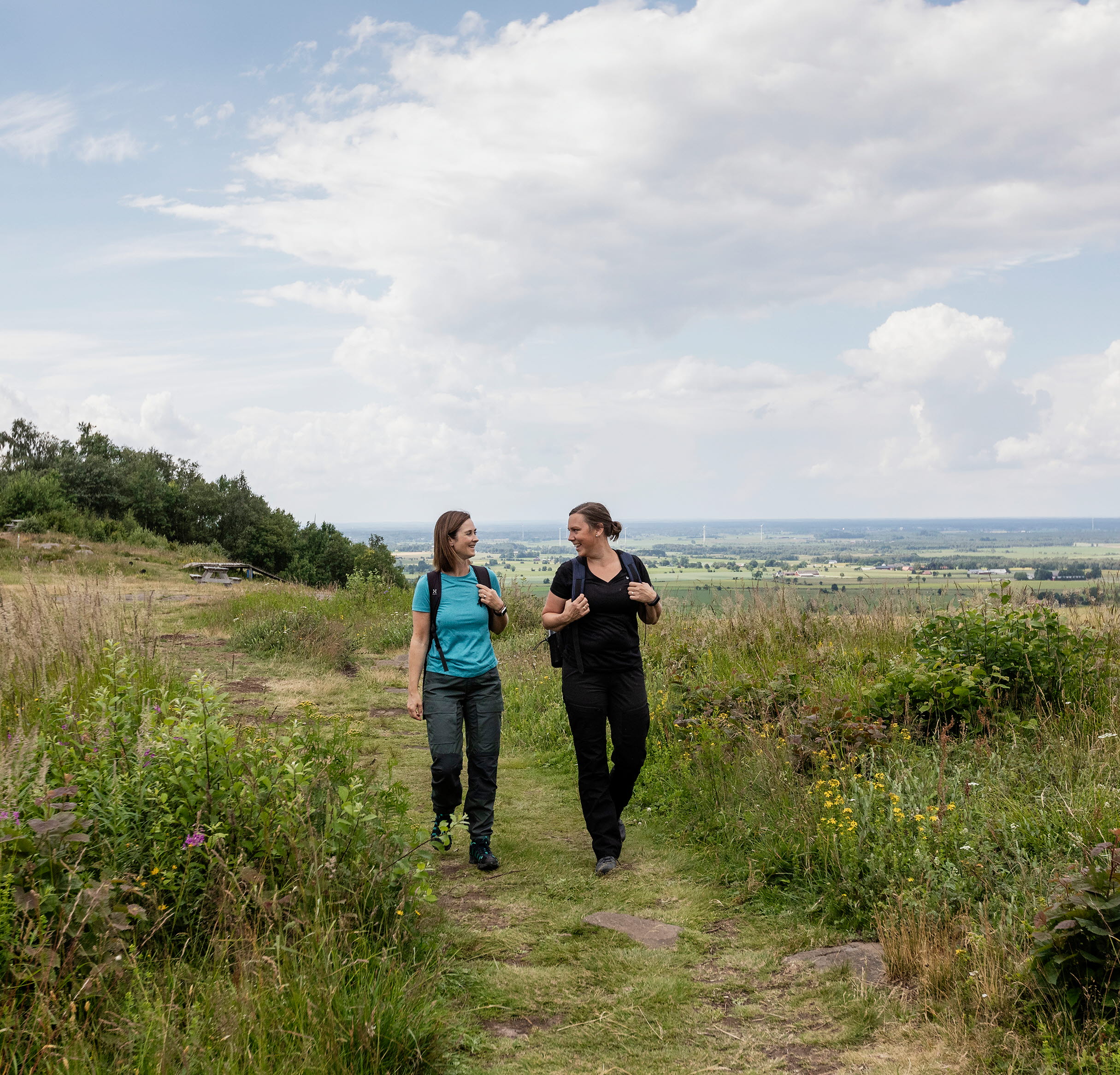 Två kvinnor som vandrar, bakom sig har de vacker utsikt från berget.
