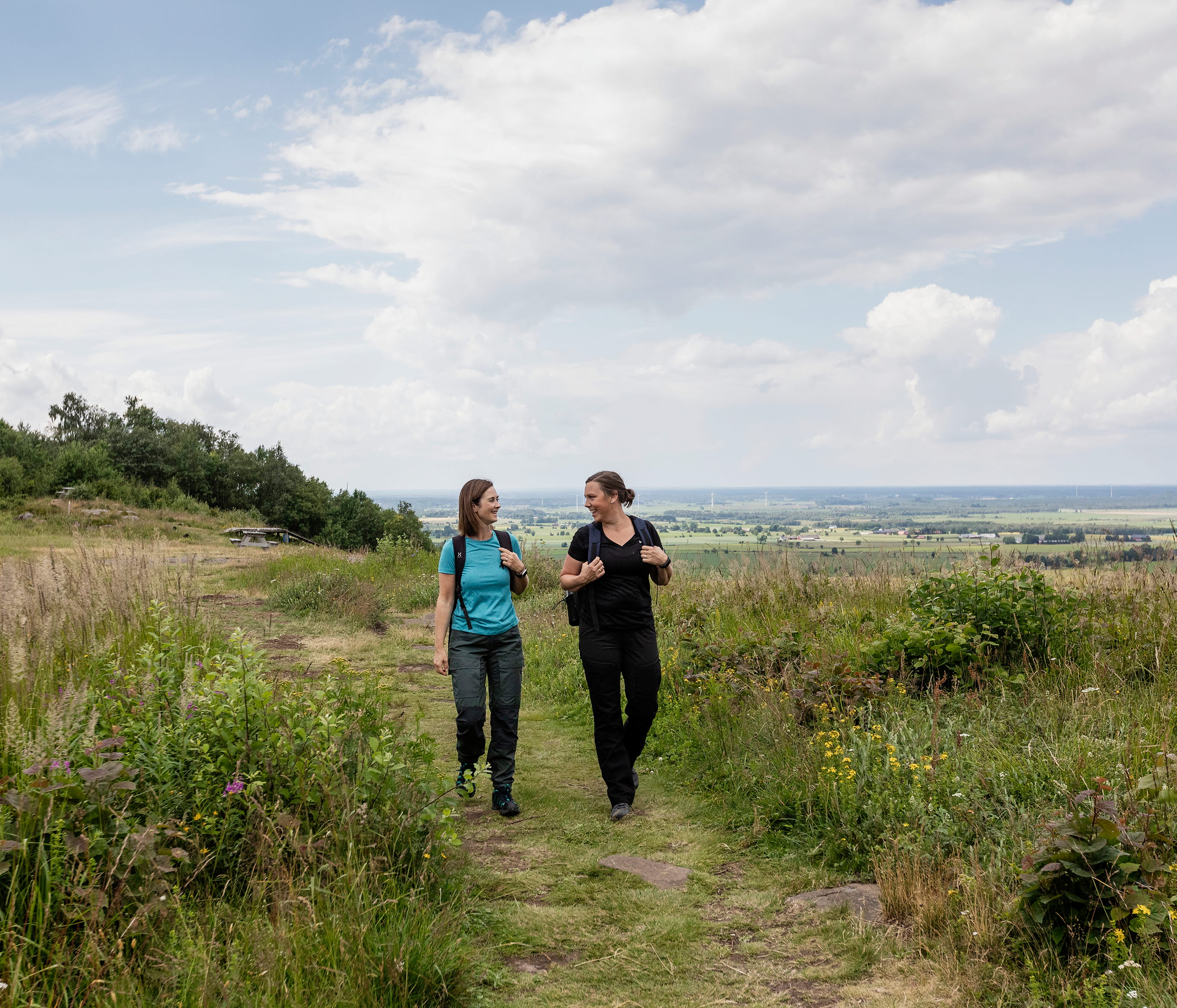 Två kvinnor som vandrar, bakom sig har de vacker utsikt från berget.