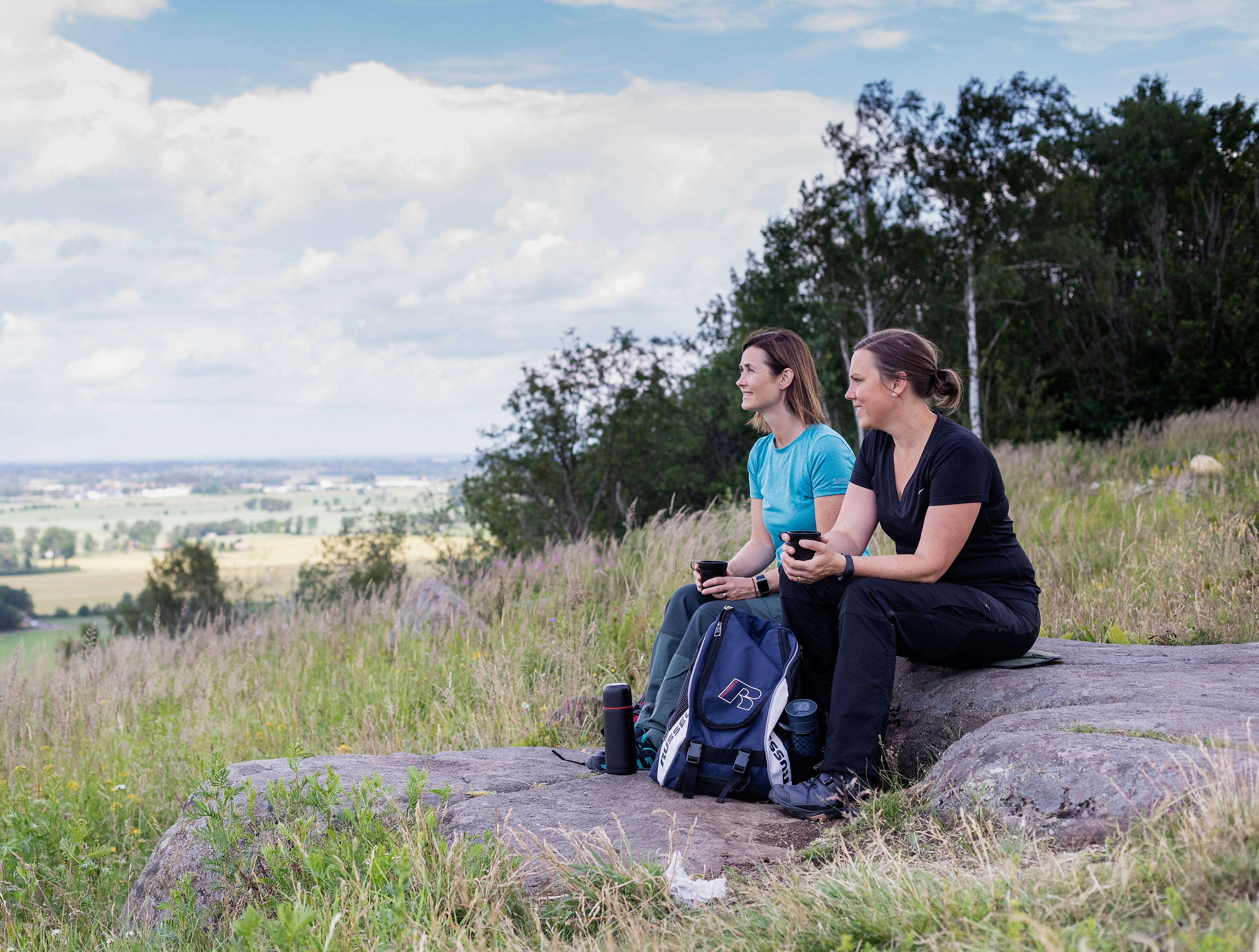 Två kvinnor som sitter på en sten och fikar och tittar på utsikten.