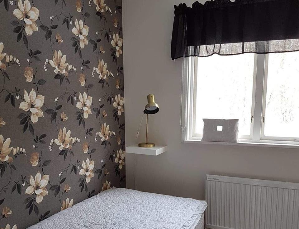 Enbäddsrum med säng och en blommig tapet i grått.