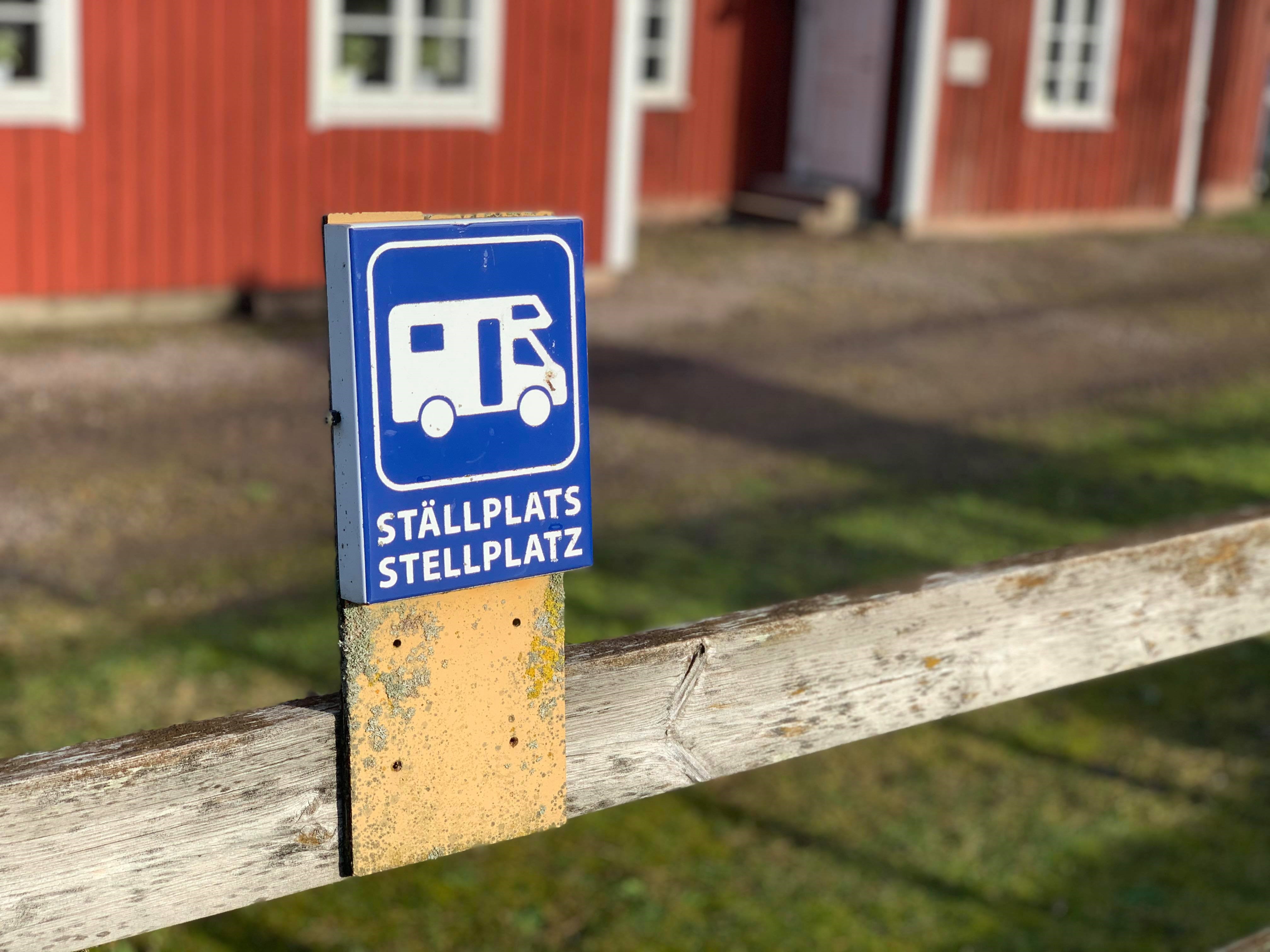 Ställplatsskylt i närbild med Café Åsle i bakgrunden.