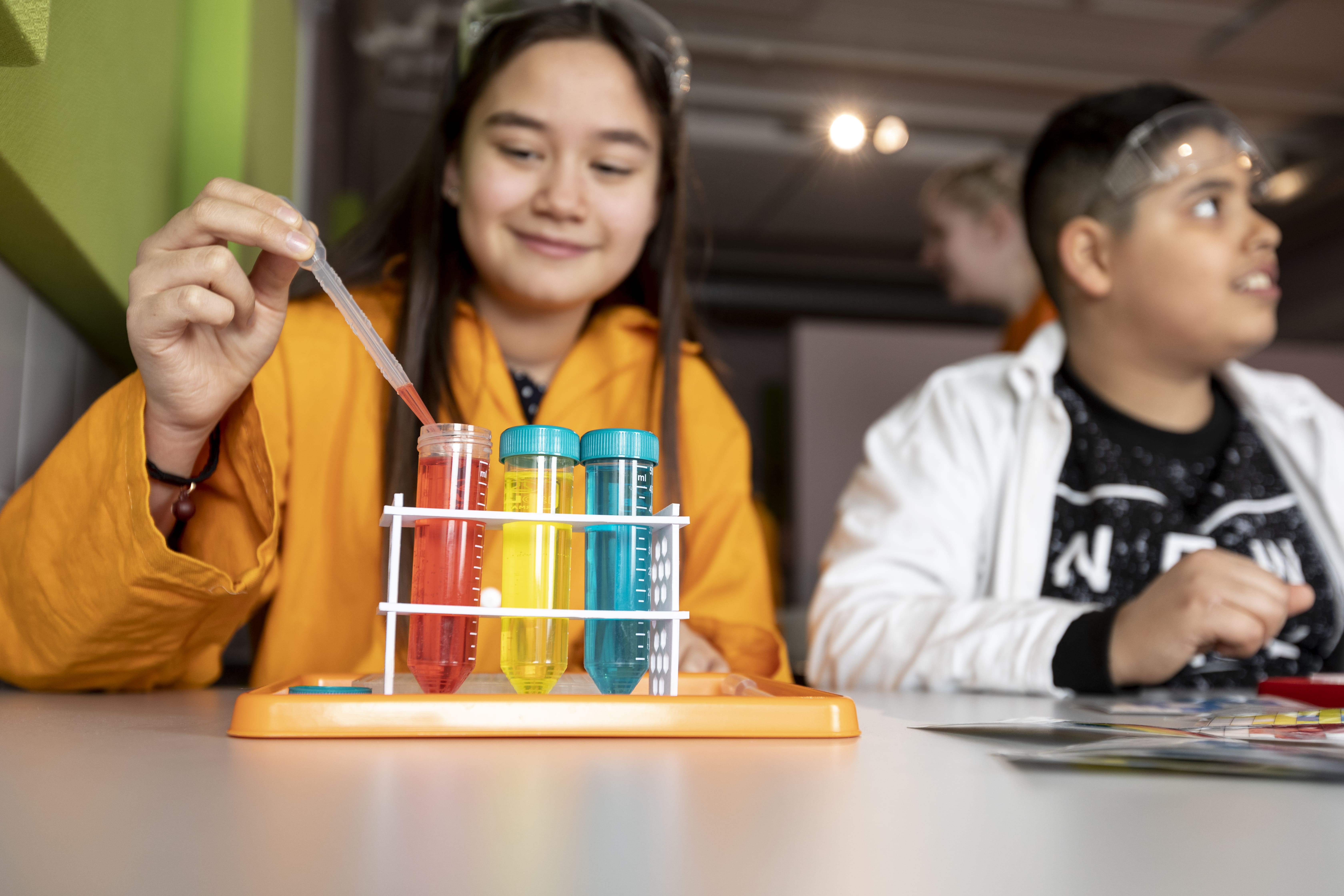 Två barn som sitter vid ett bord och gör ett experiment med provrör med olika färger.