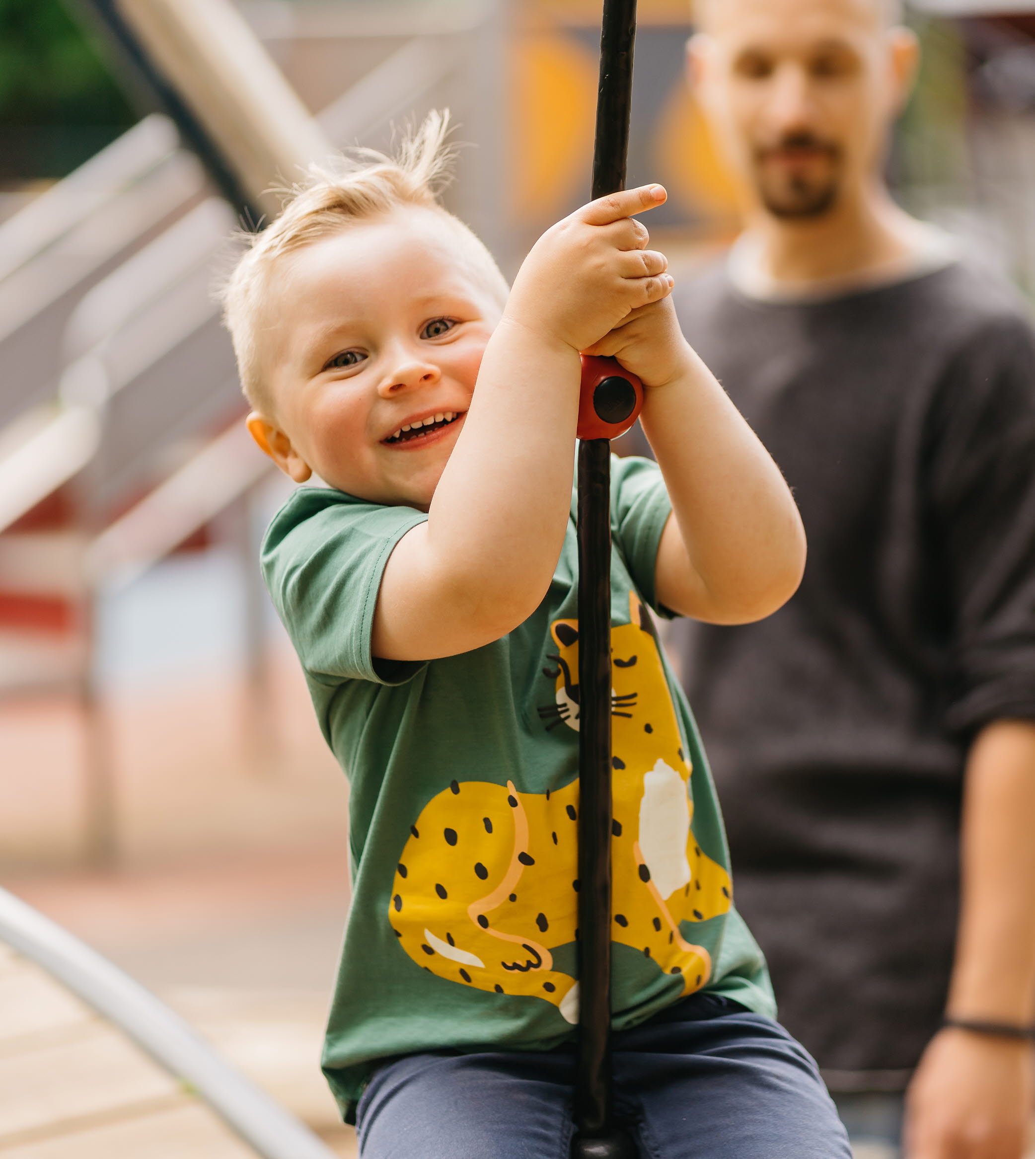 Pojke som åker linbana, pappan står i bakgrunden.