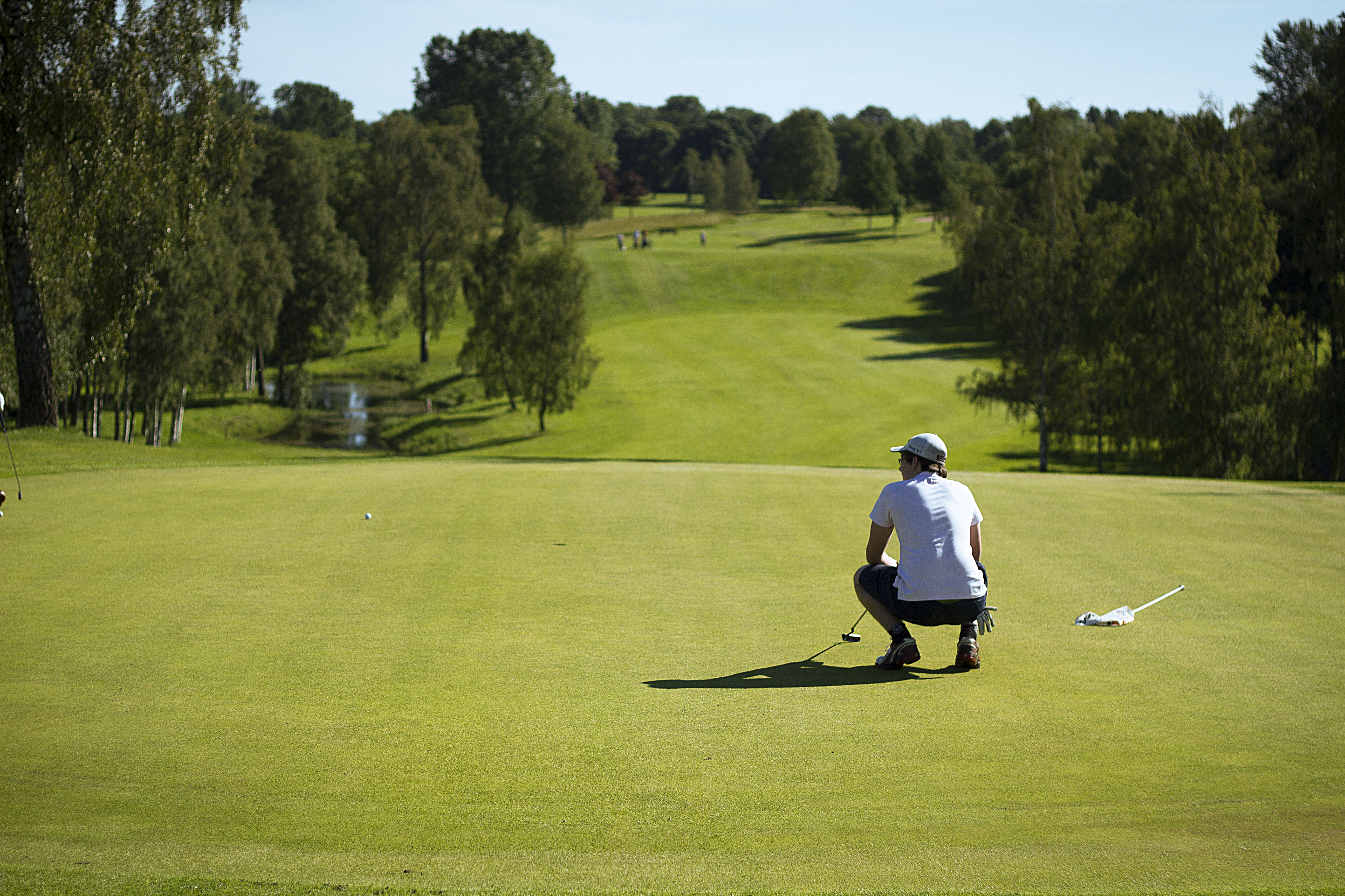 Man som sitter på huk och ser ut över golfbanan.