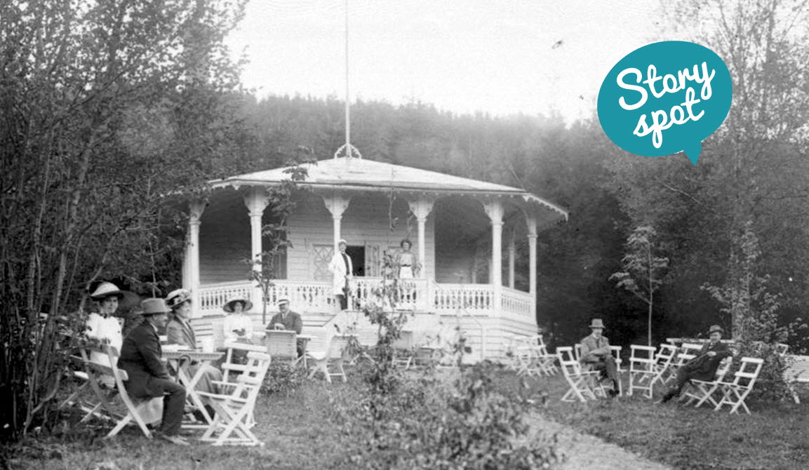 Svart/vitt gammalt foto med människor som sitter utanför en paviljong.