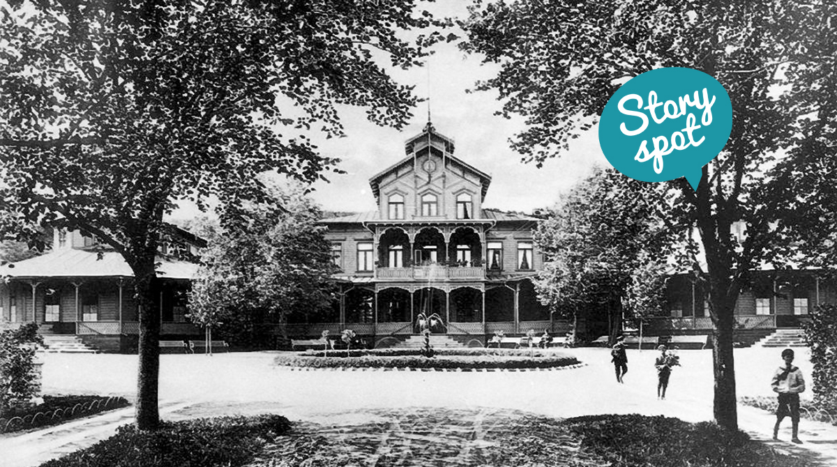 Svart/vit gammal bild på ett stort trähus med snickarglädje. Tre personer syns också på kortet.