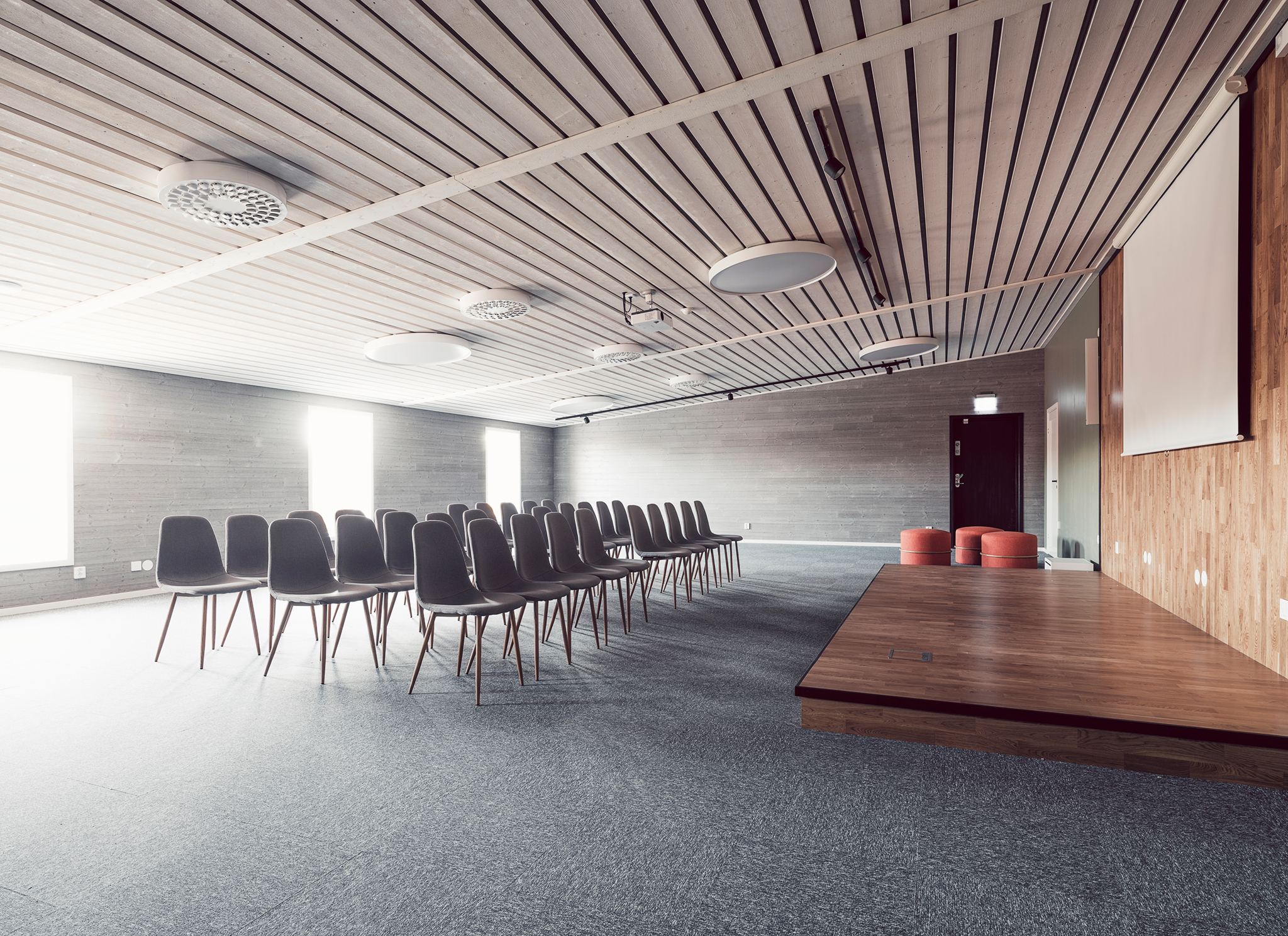 Stort konferensrum med svarta solar i tre rader och ett podium där talaren kan stå. 