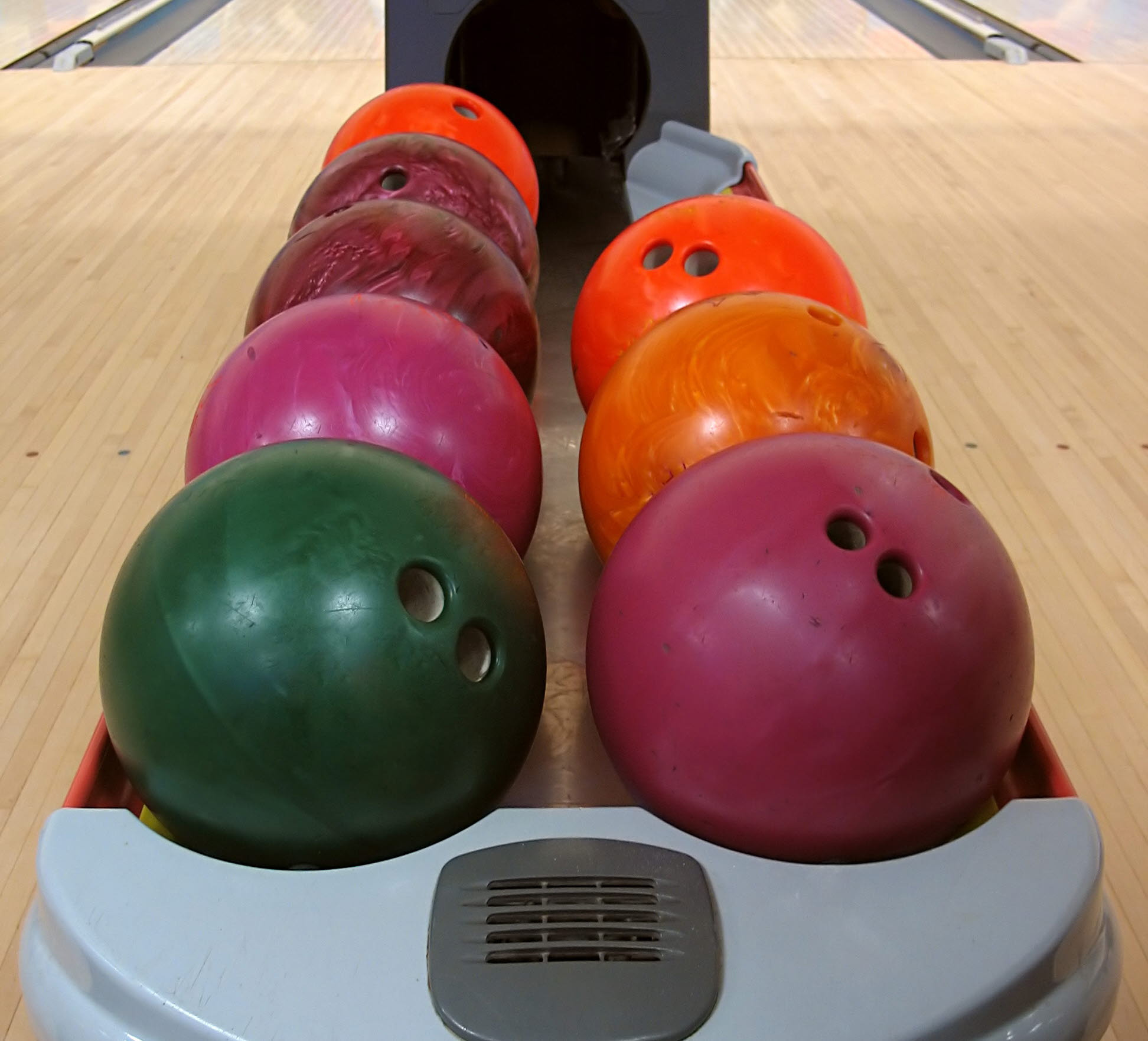 Bowlingklot i olika färger som ligger på en skena. Bowlingbanan syns i bakgrunden.