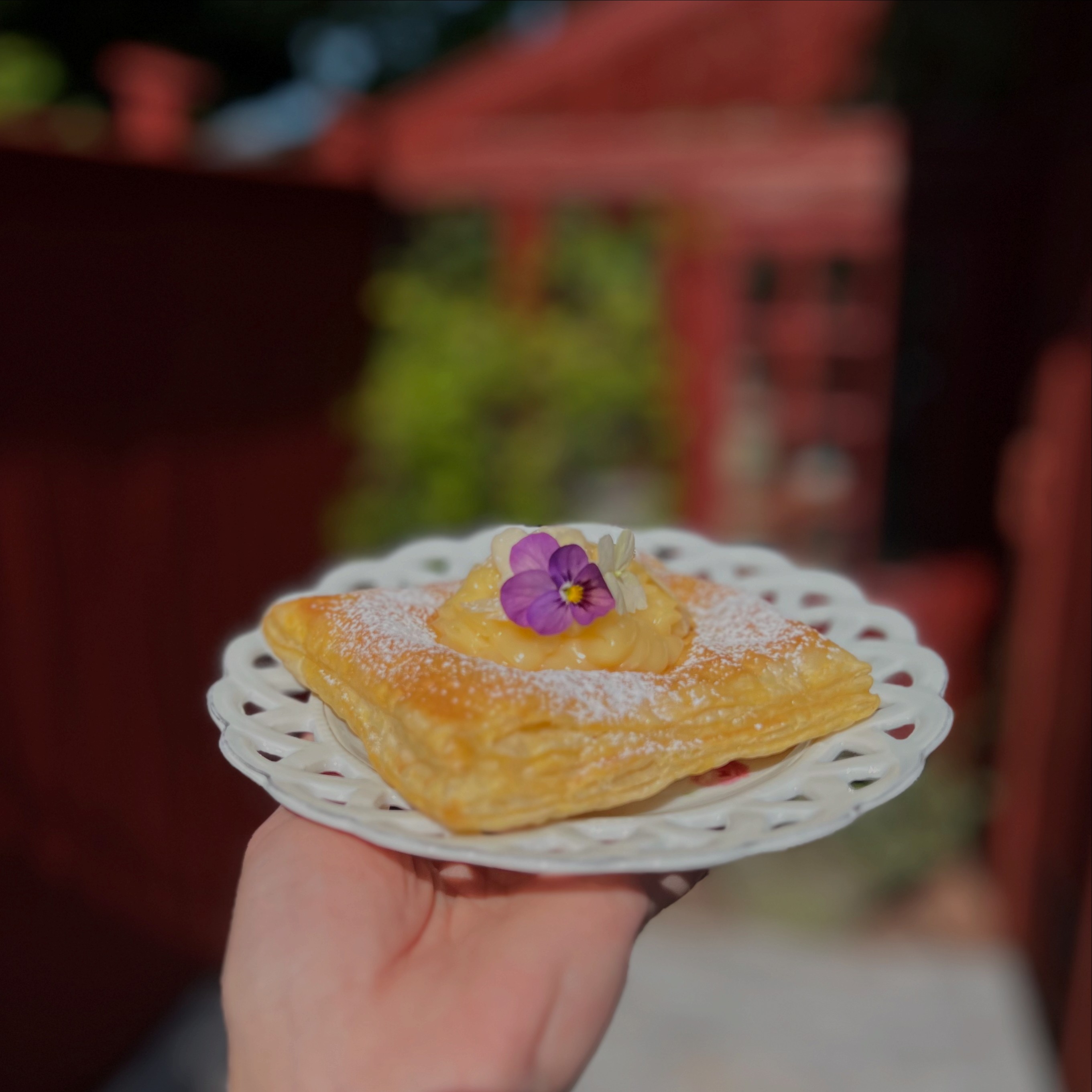 En kaka med en lila blomma på toppen. fatet hålls av en hand.