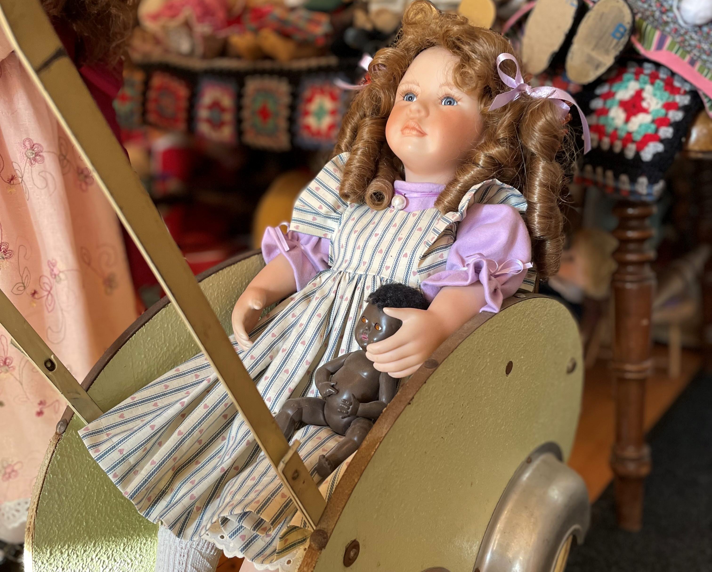 En docka som sitter i en gammaldags dockvagn.