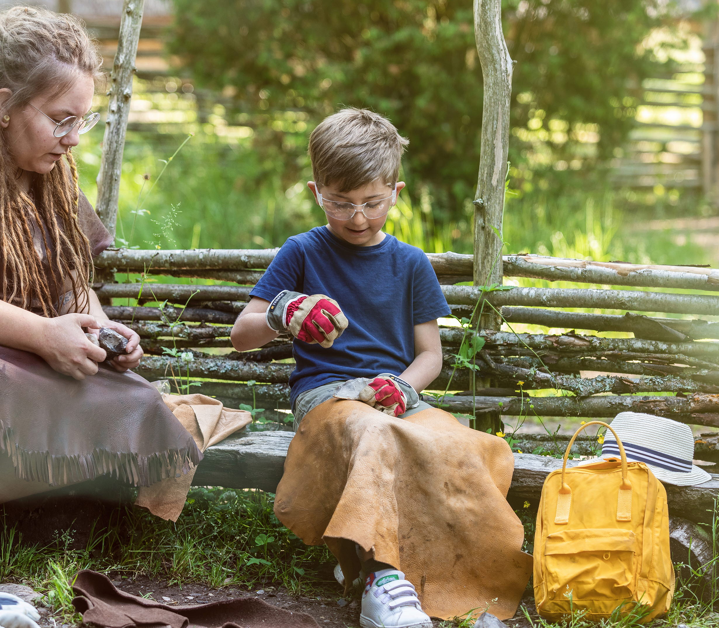 Pojke som sitter och slår flinta tillsammans med en kvinna i stenålderskläder.