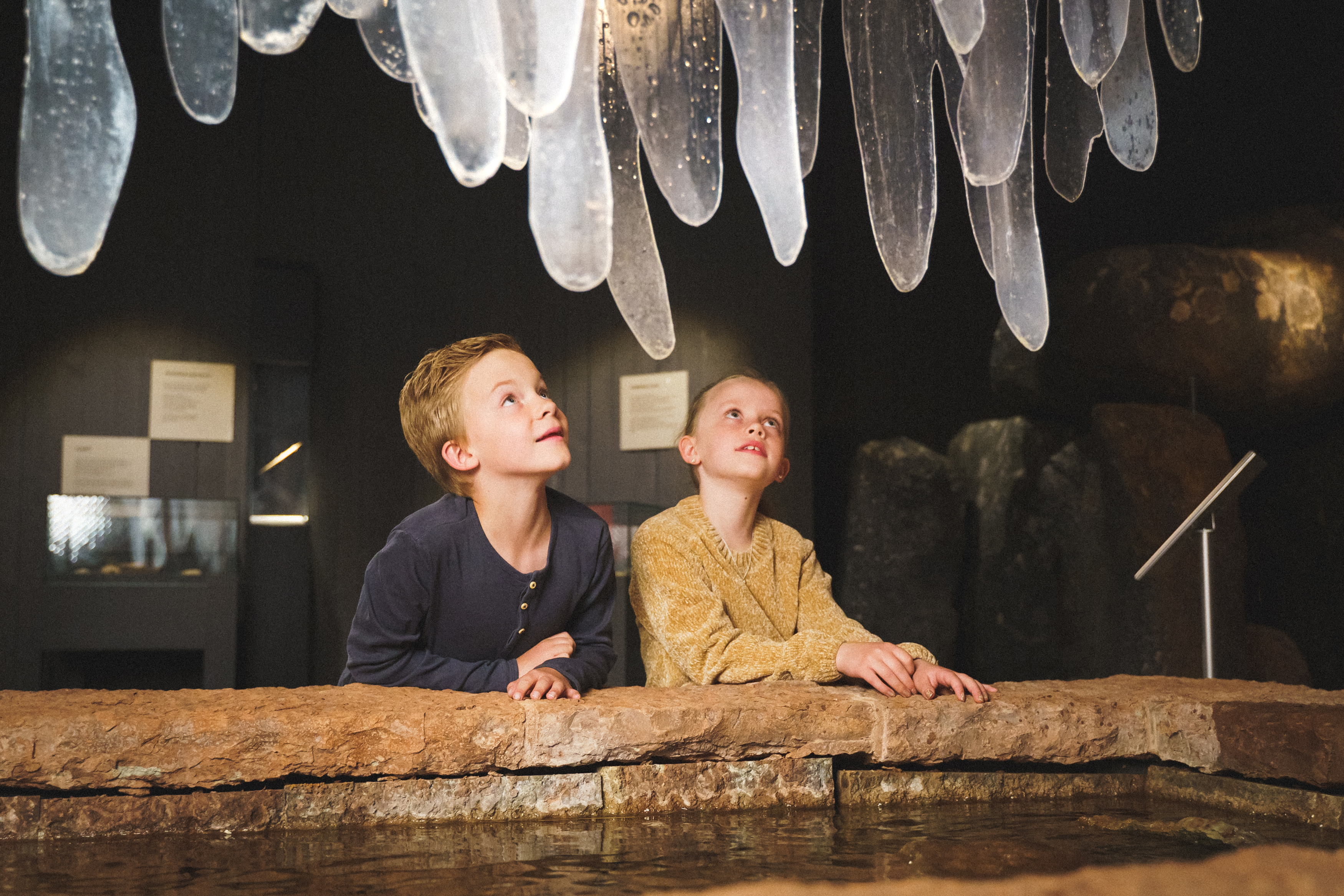 En pojke och en flicka står och kikar på is som droppar från taket i en utställning på museet.