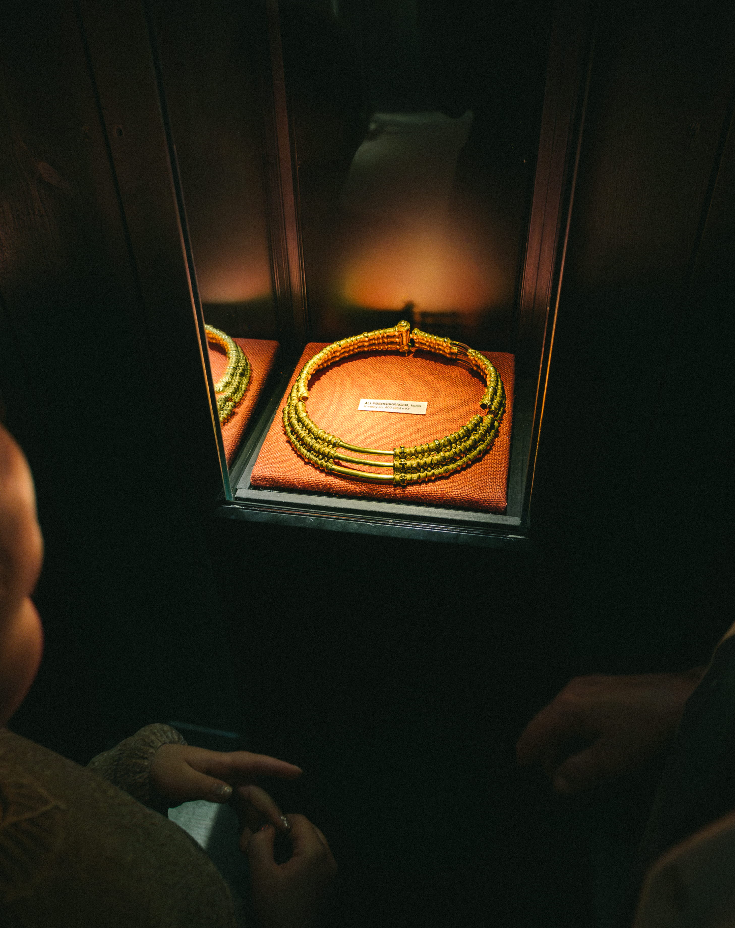 Ett barn och en kvinna som tittar på en guldkrage, det är mörkt i rummet men kragen är upplyst.