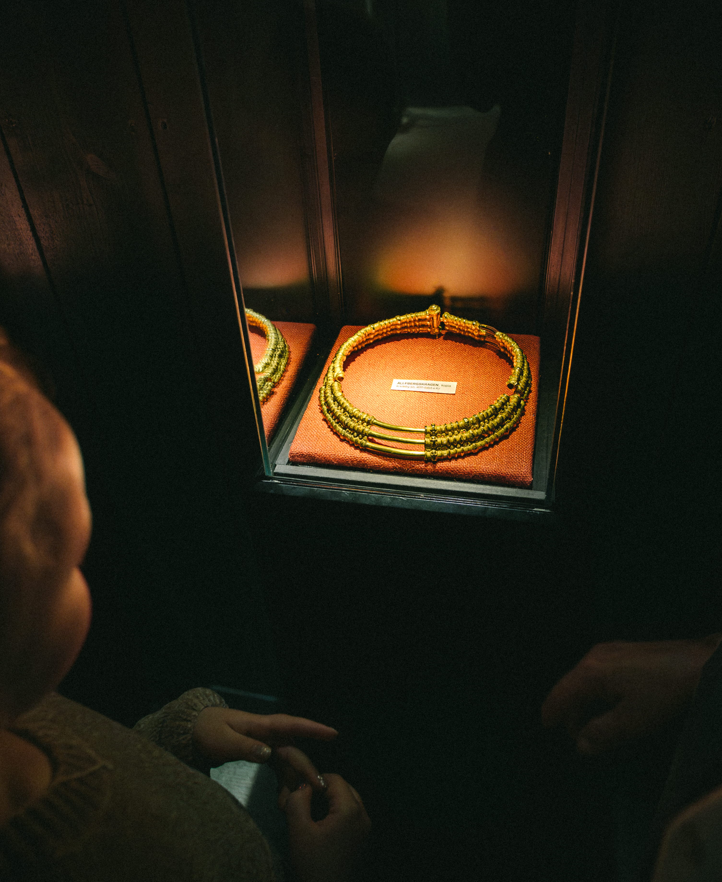 Ett barn och en kvinna som tittar på en guldkrage, det är mörkt i rummet men kragen är upplyst.