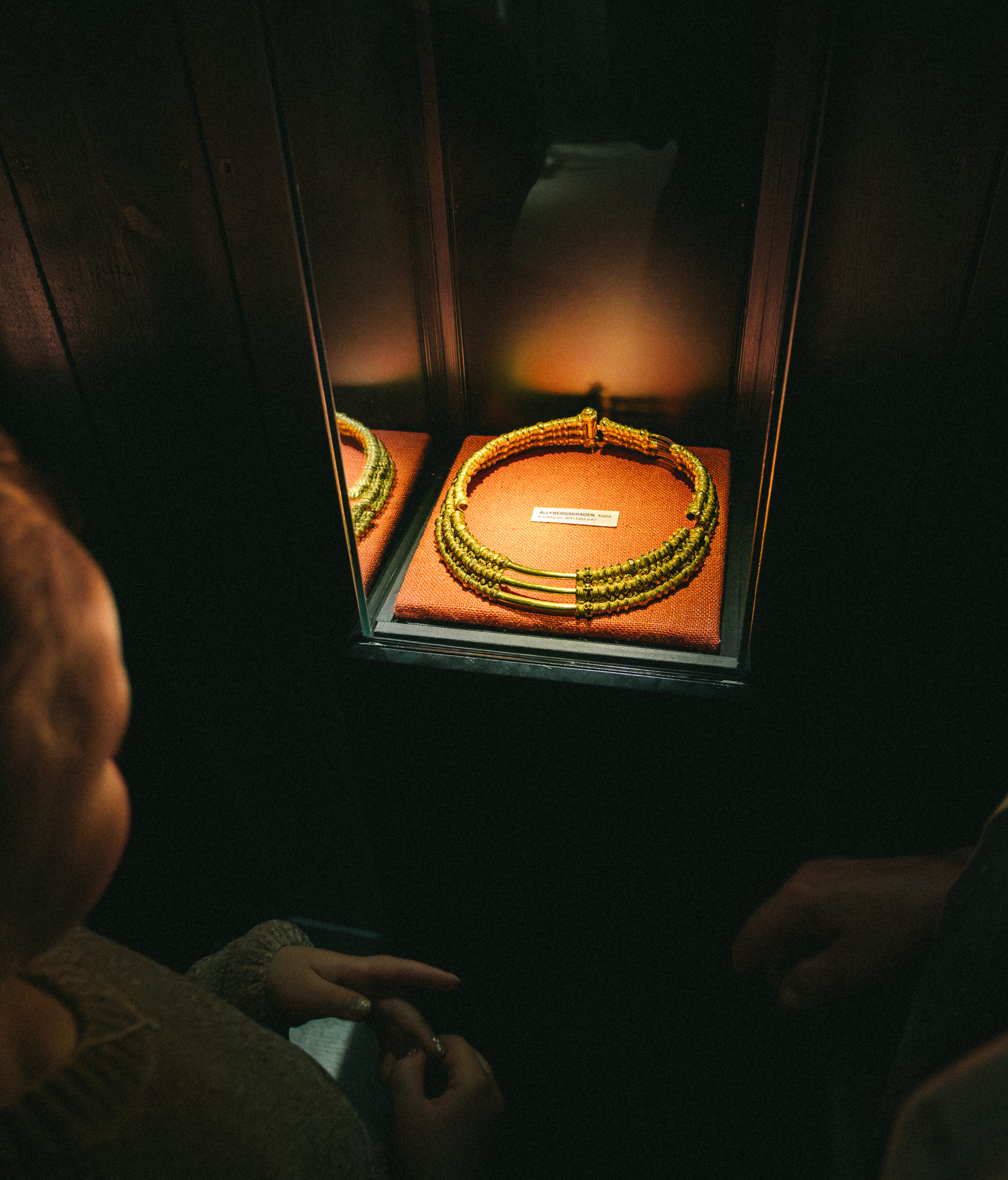 Ett barn och en kvinna som tittar på en guldkrage, det är mörkt i rummet men kragen är upplyst.