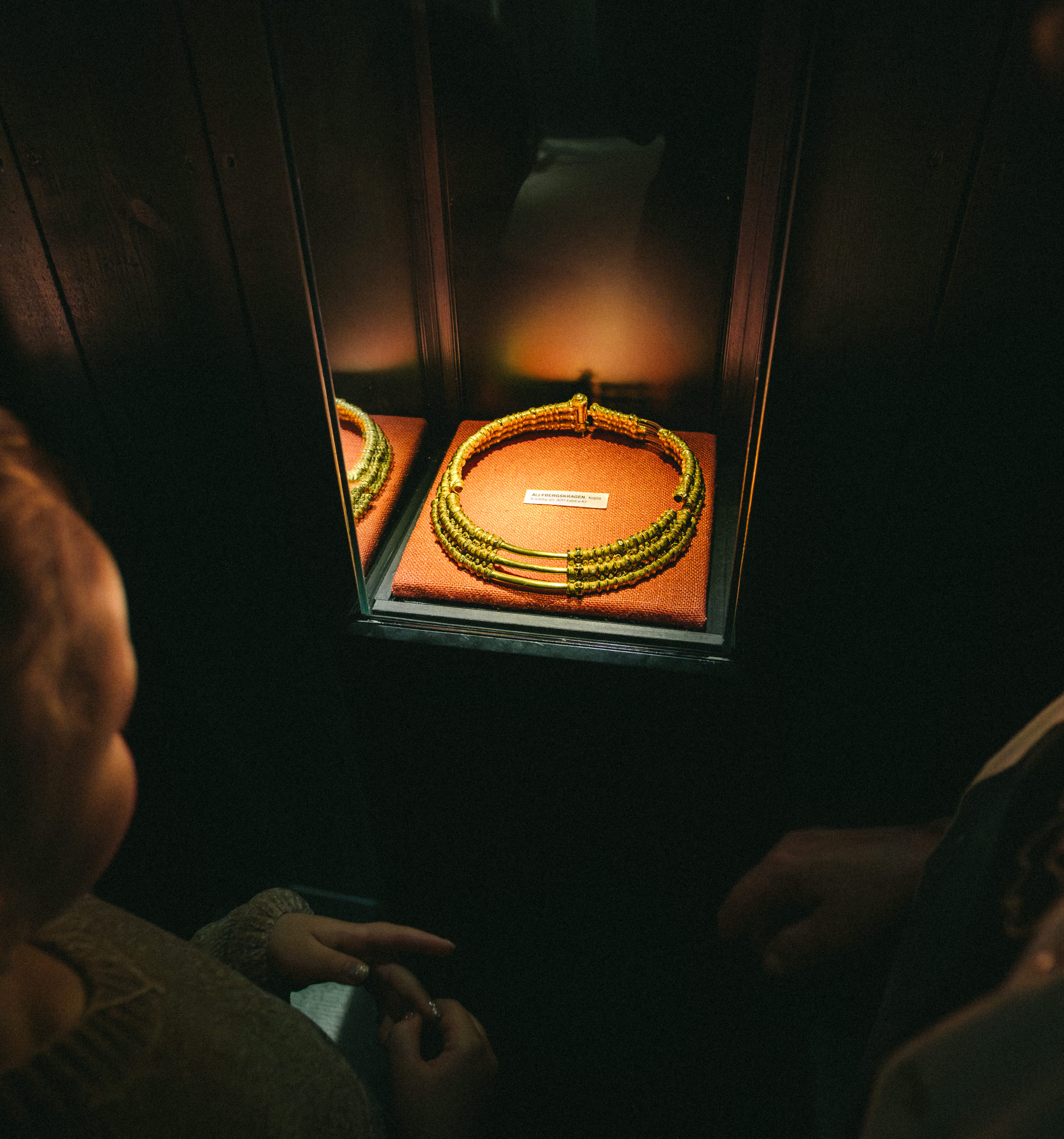 Ett barn och en kvinna som tittar på en guldkrage, det är mörkt i rummet men kragen är upplyst.