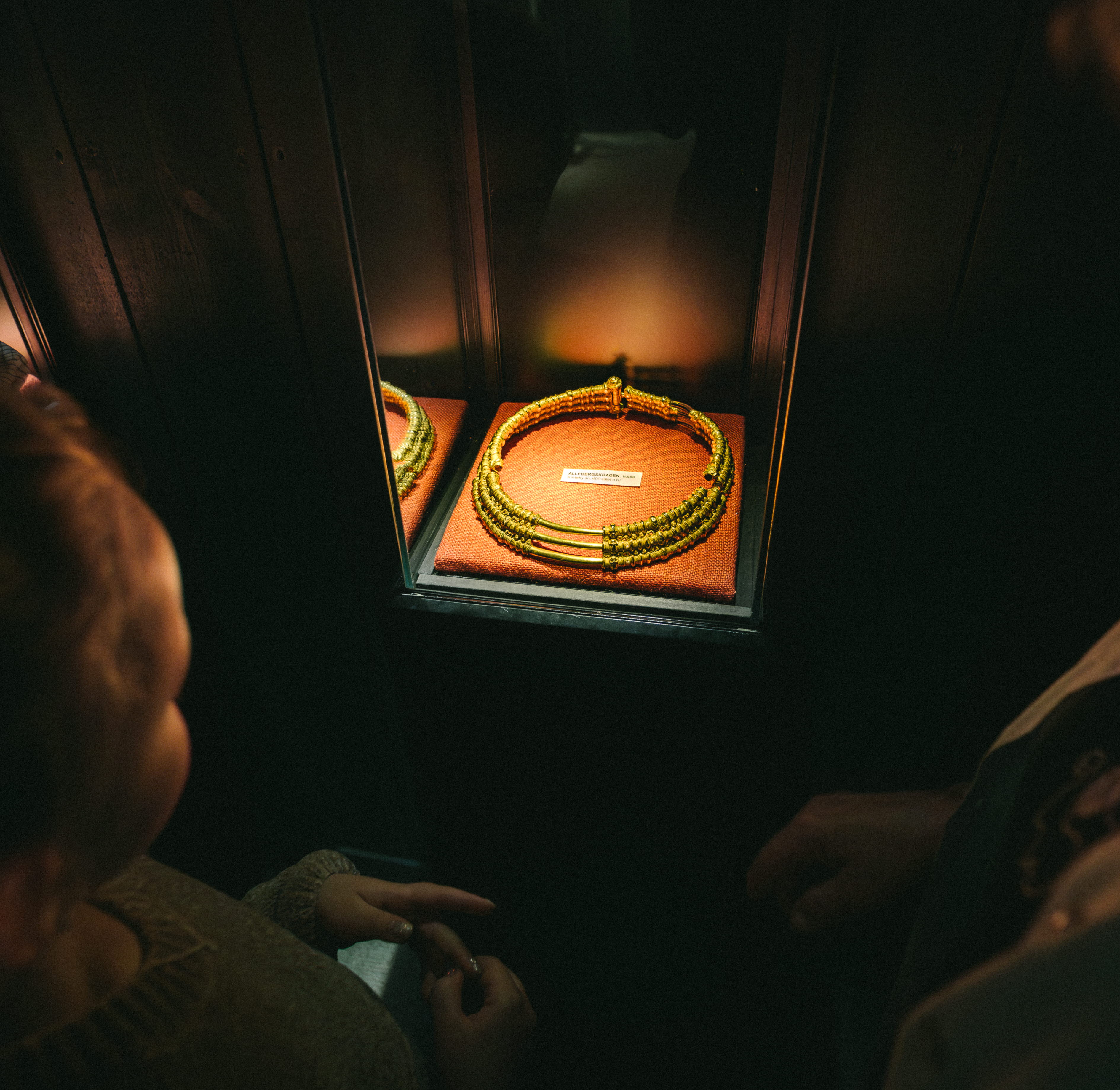 Ett barn och en kvinna som tittar på en guldkrage, det är mörkt i rummet men kragen är upplyst.