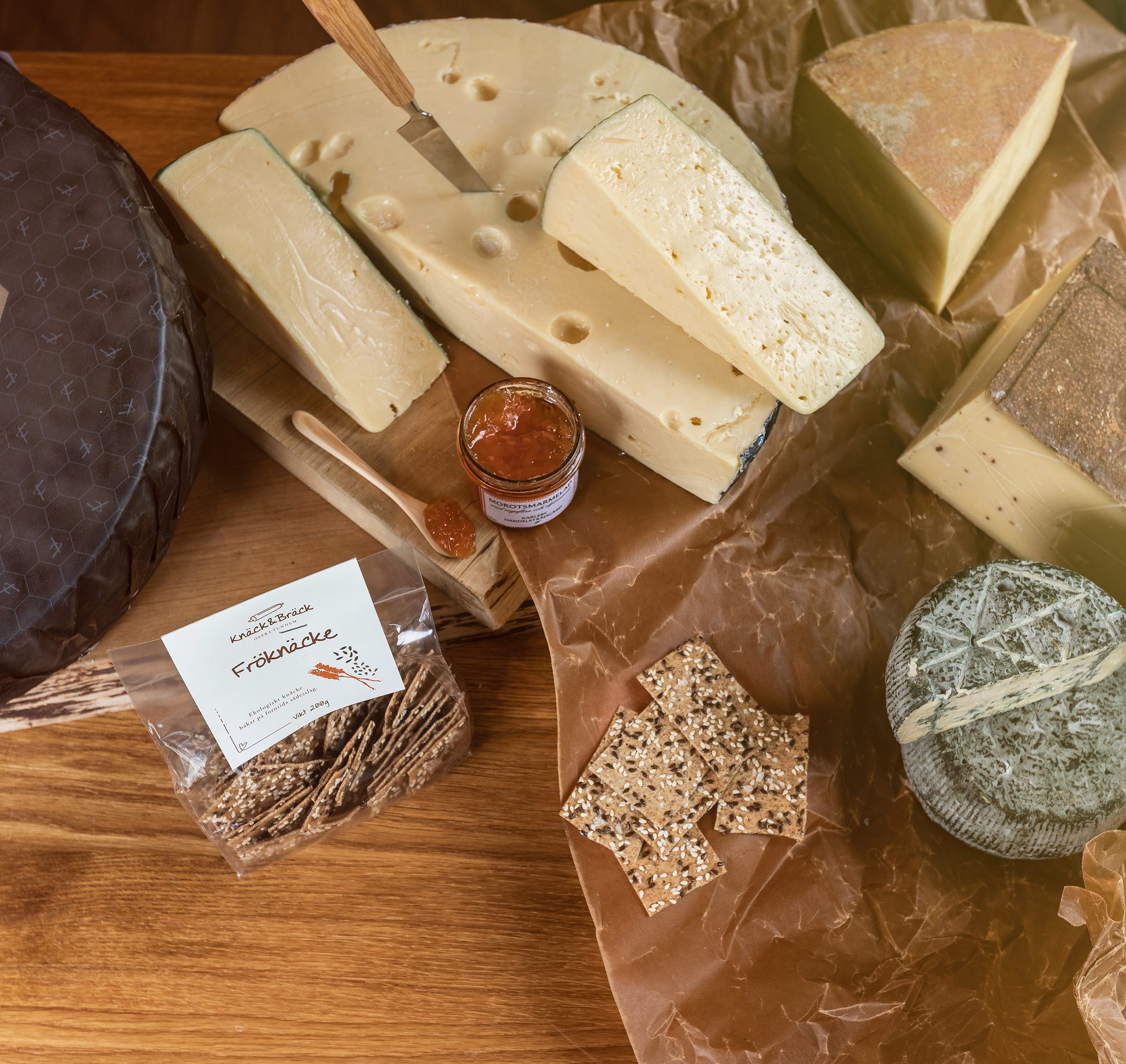 Olika sorters ostar på ett bord. Även knäckebröd med frön och en hel ost med svart förpackning där det står Falbygdens Osteria.