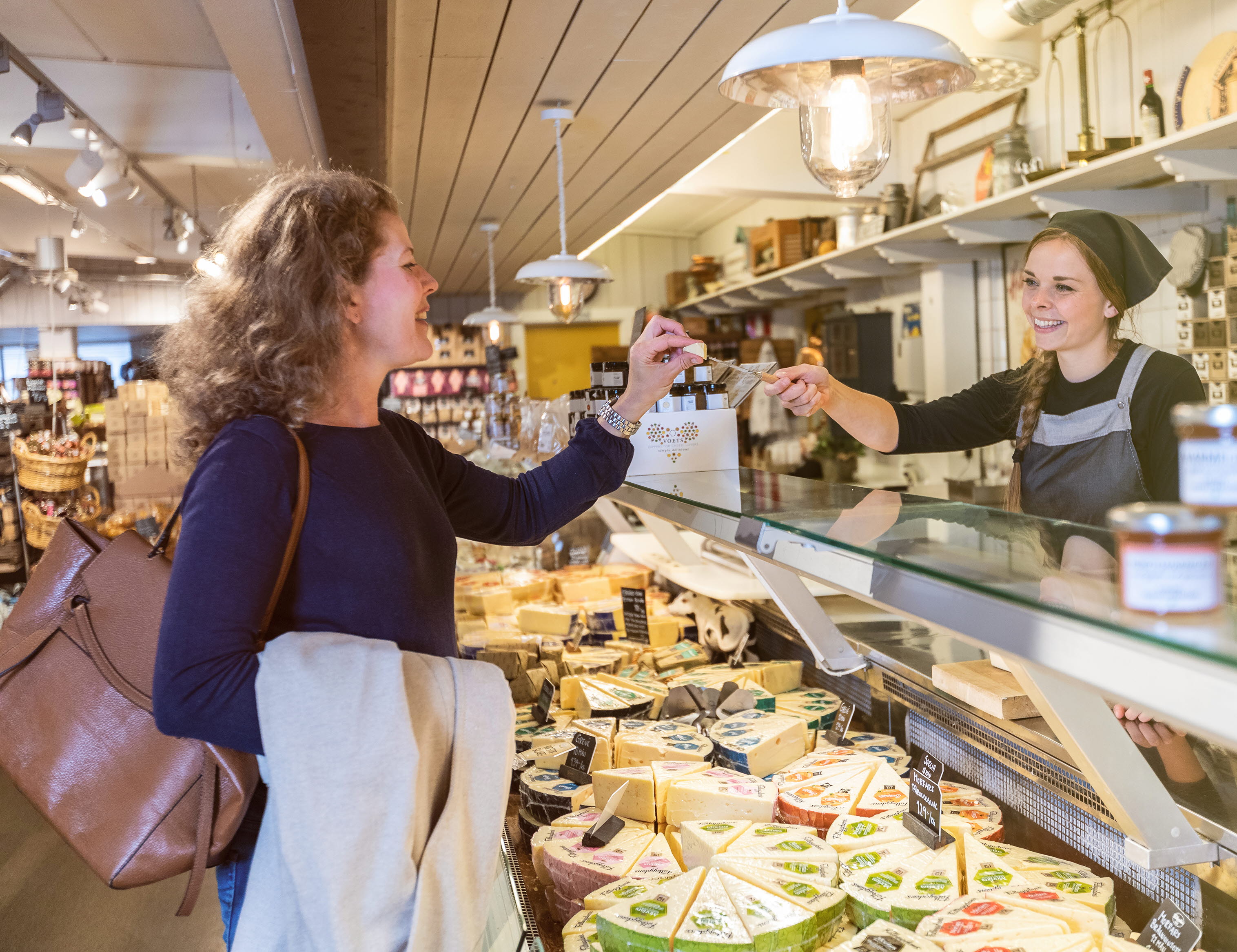 Kvinna som provsmakar en ostbit som expediten ger henne över en ostdisk.