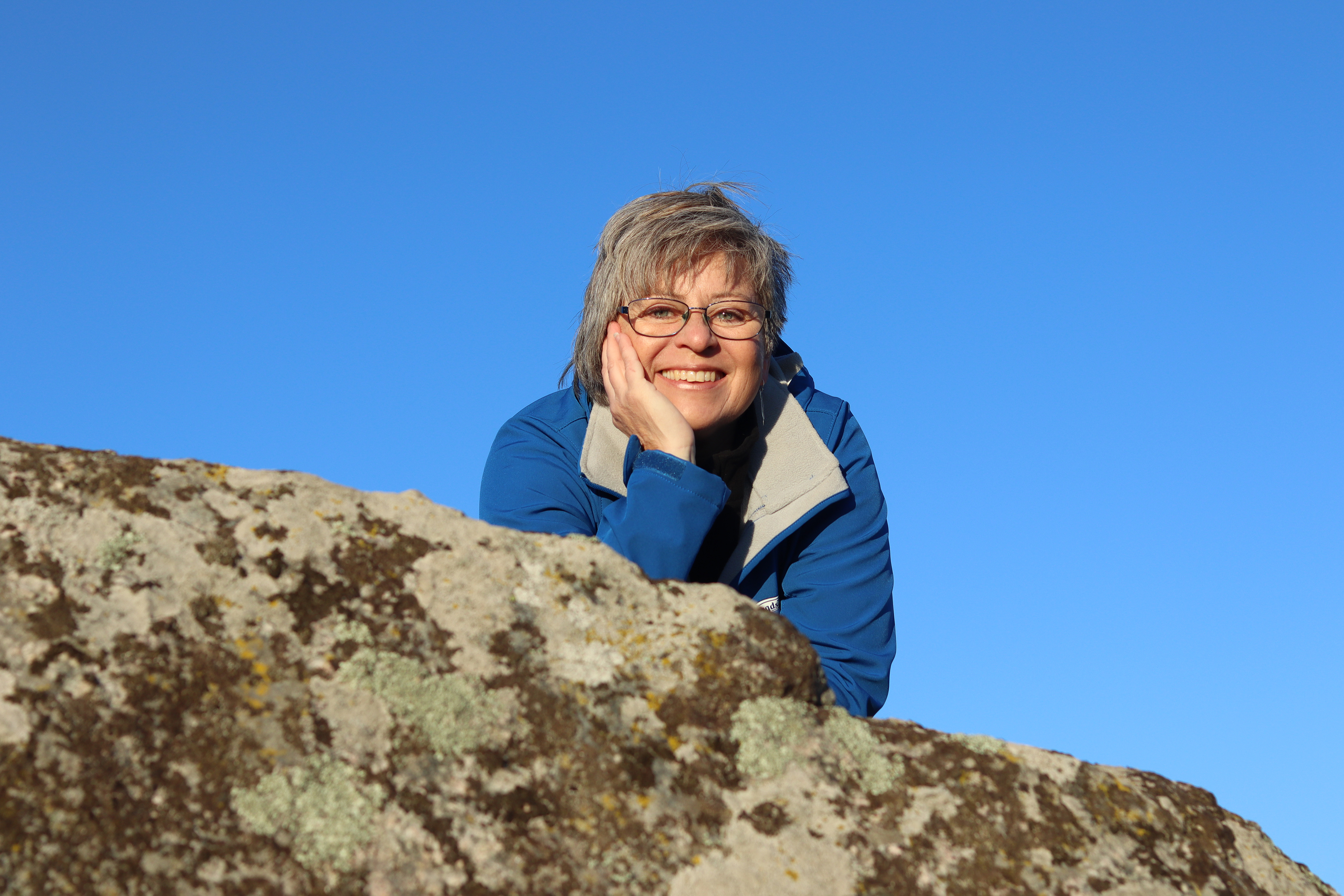 Kvinna som sticker fram överkroppen över en sten och ler.