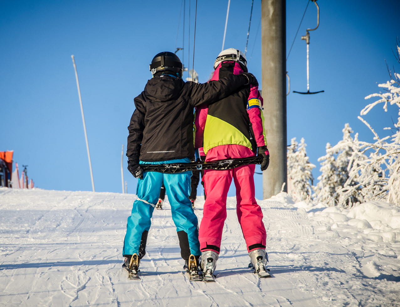 Two children riding a lift with their backs to the camera. Colorful clothes.