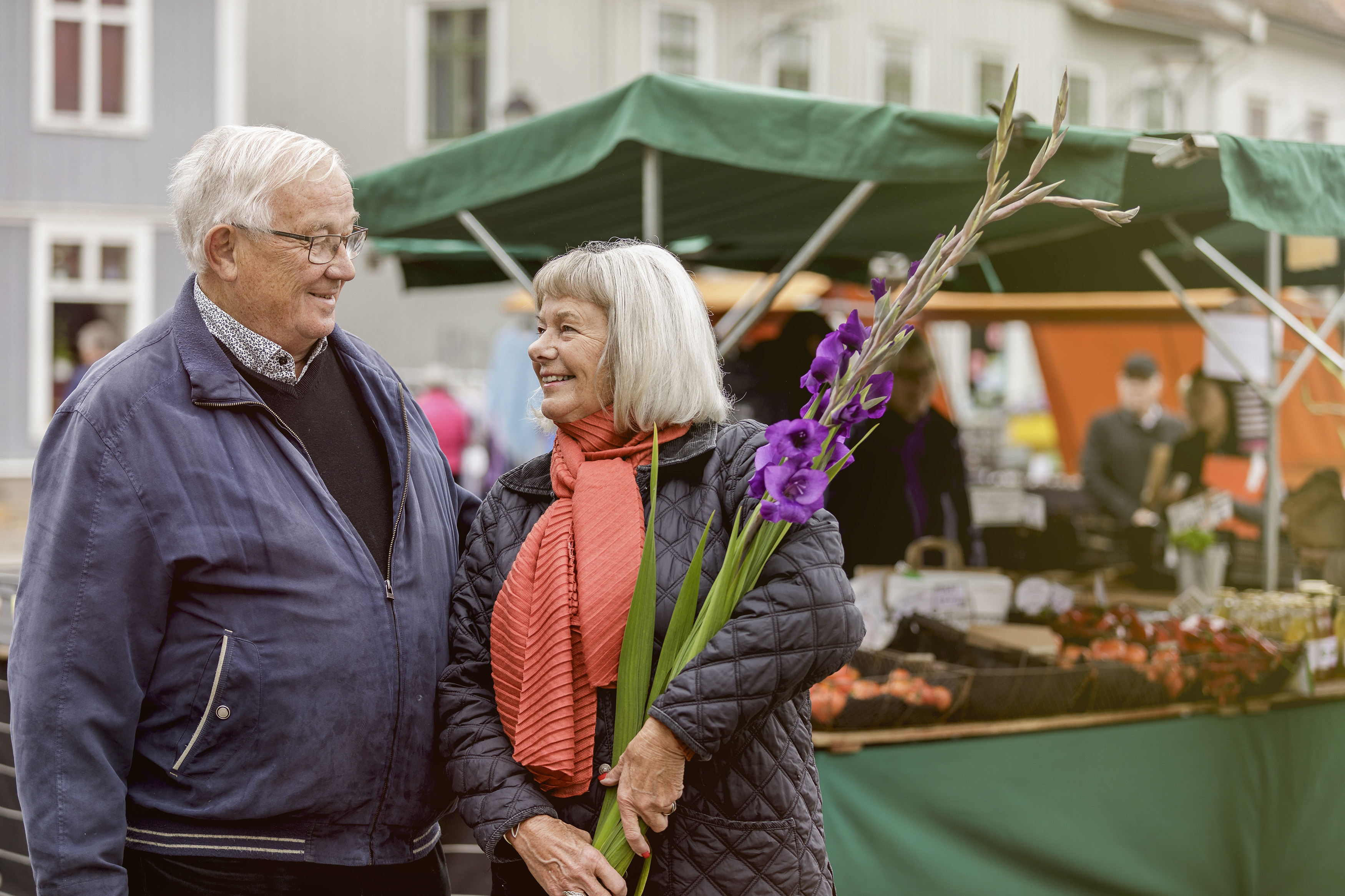 Man och kvinna som tittar på varandra. kvinnan har blommor i famnen och i bakgrunden syns en marknad.