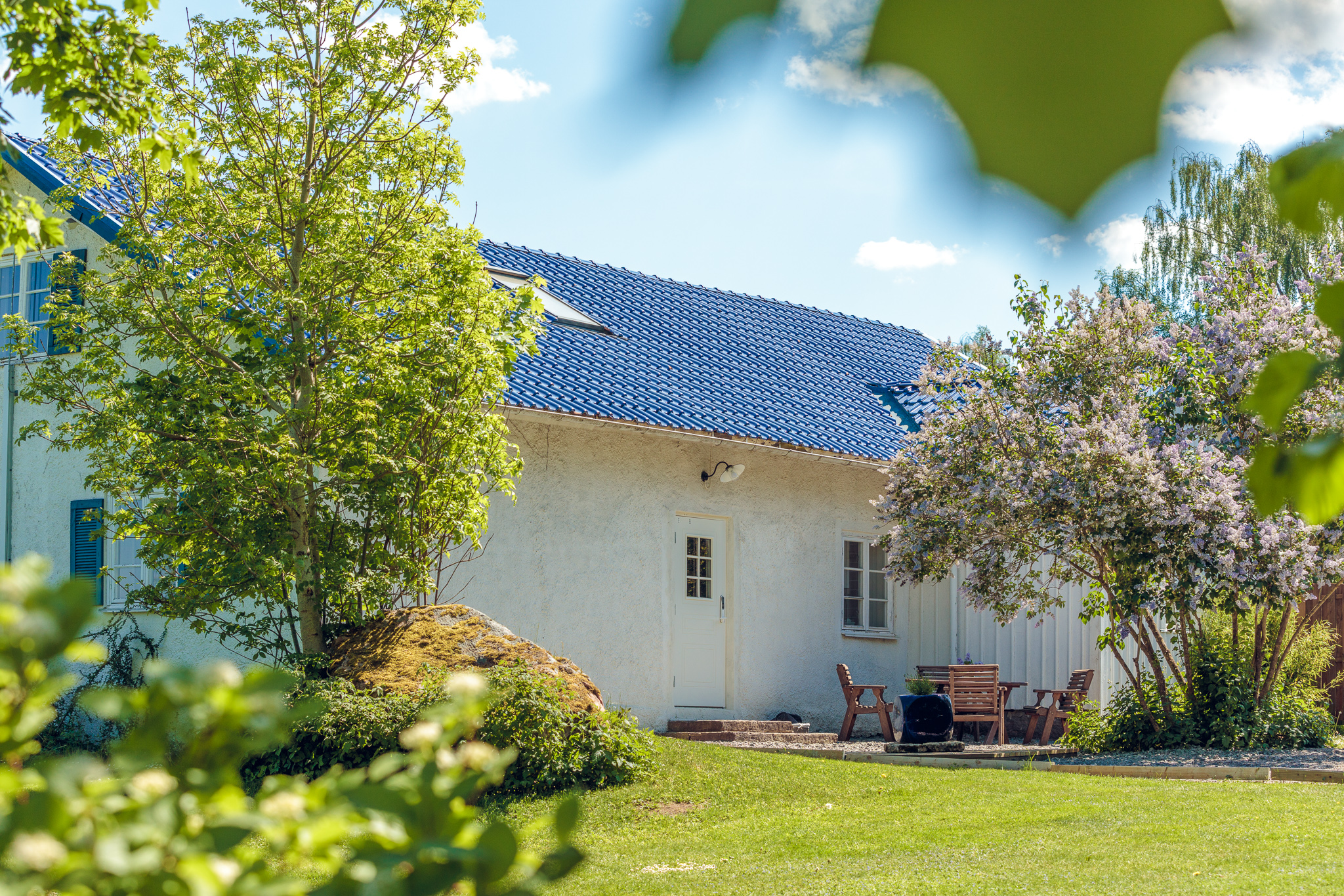 Vitt hus med trädgårdsmöbler framför. Grönt gräs och några träd.