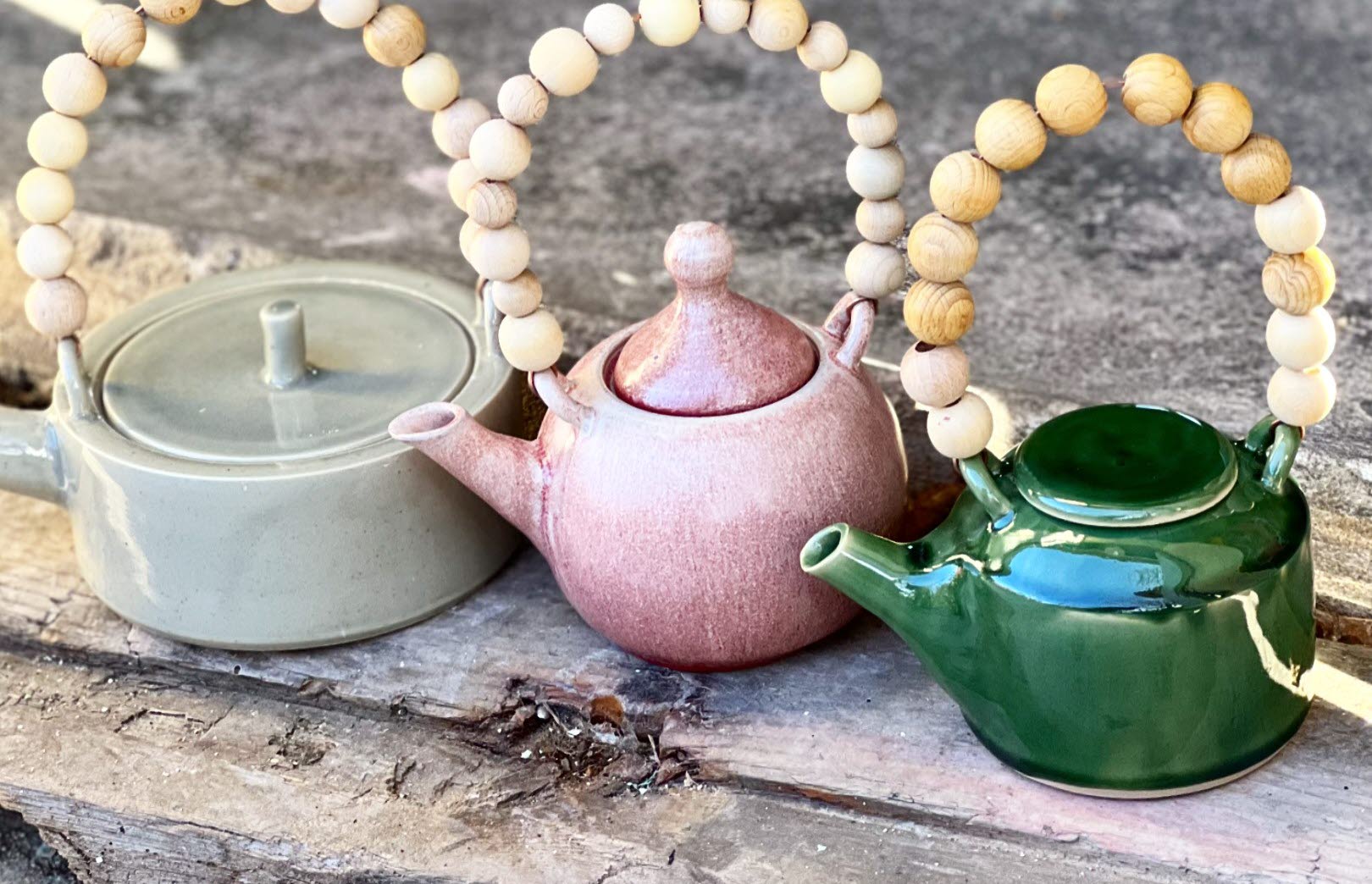 Tre tekannor i olika färg av keramik. De har trähandtag av kulor.