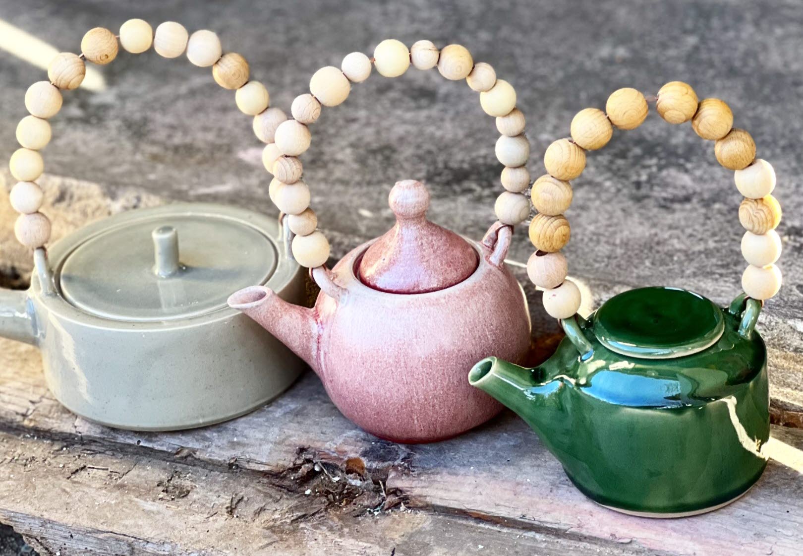Tre tekannor i olika färg av keramik. De har trähandtag av kulor.