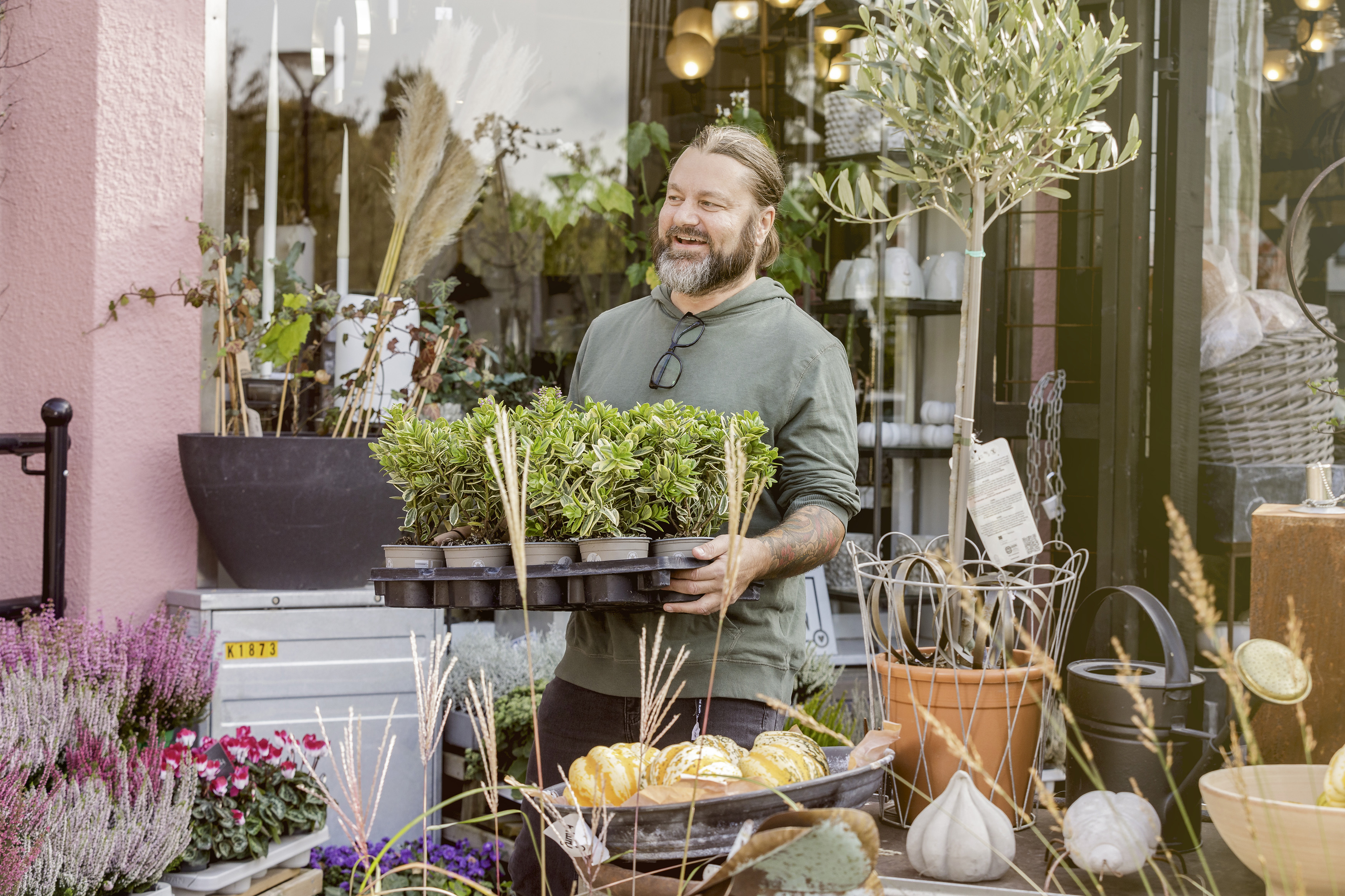Man carrying a tray with lots of plants outside a flower shop.