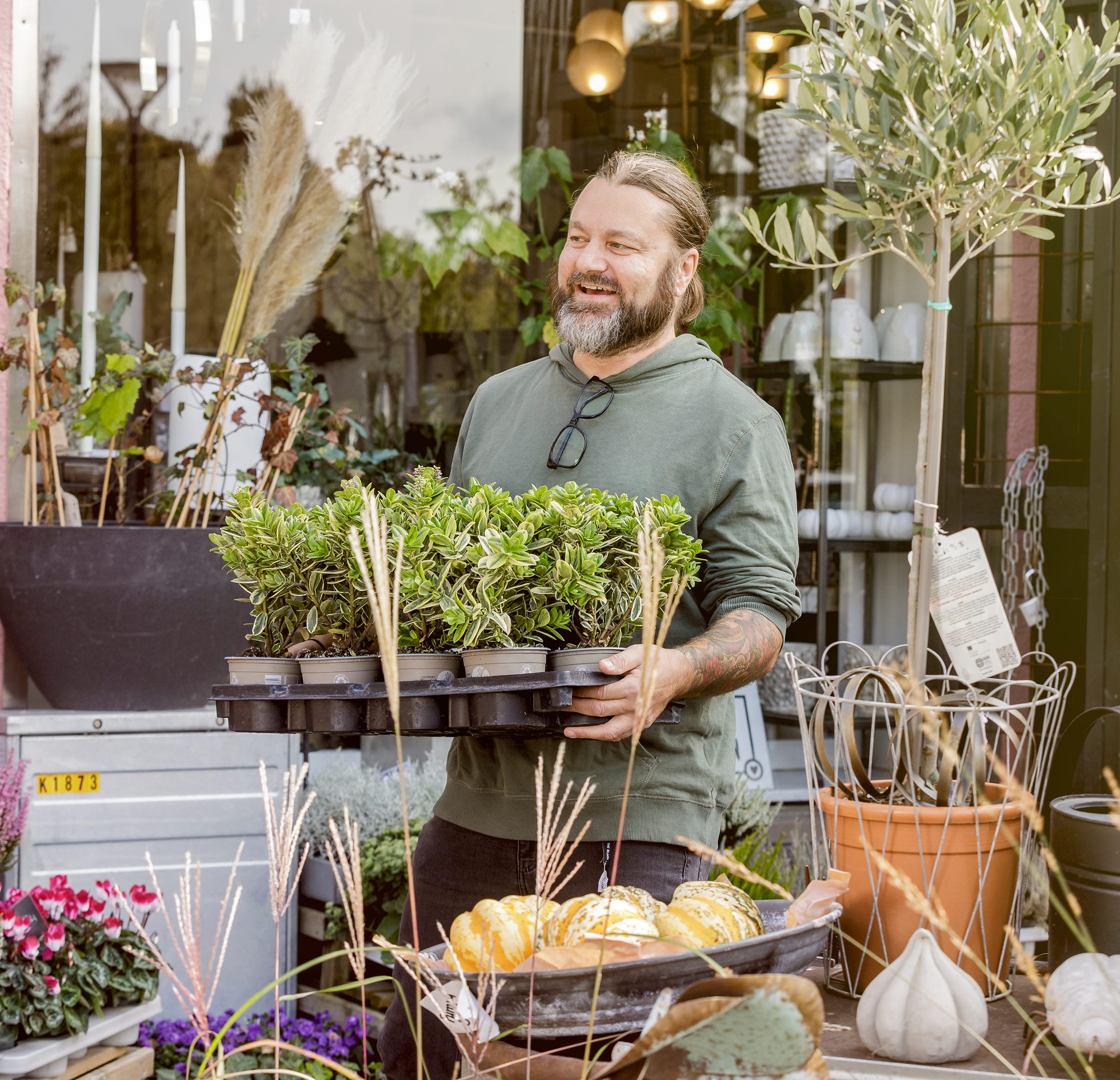 Man som bär på en bricka med massa växter utanför en blomsterbutik.