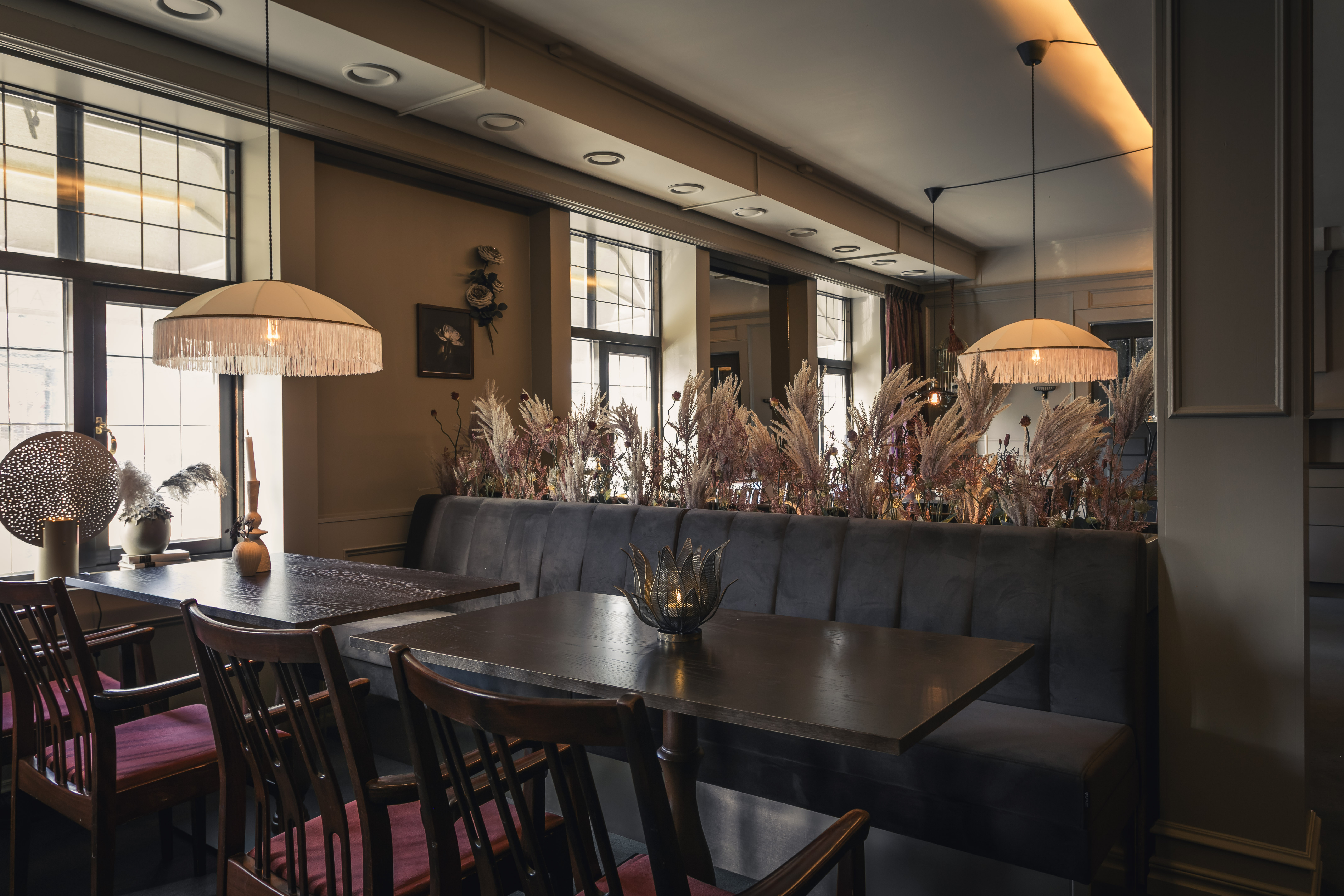 en matsal med mörka soffor i tyg och ljusa lampor över borden. 