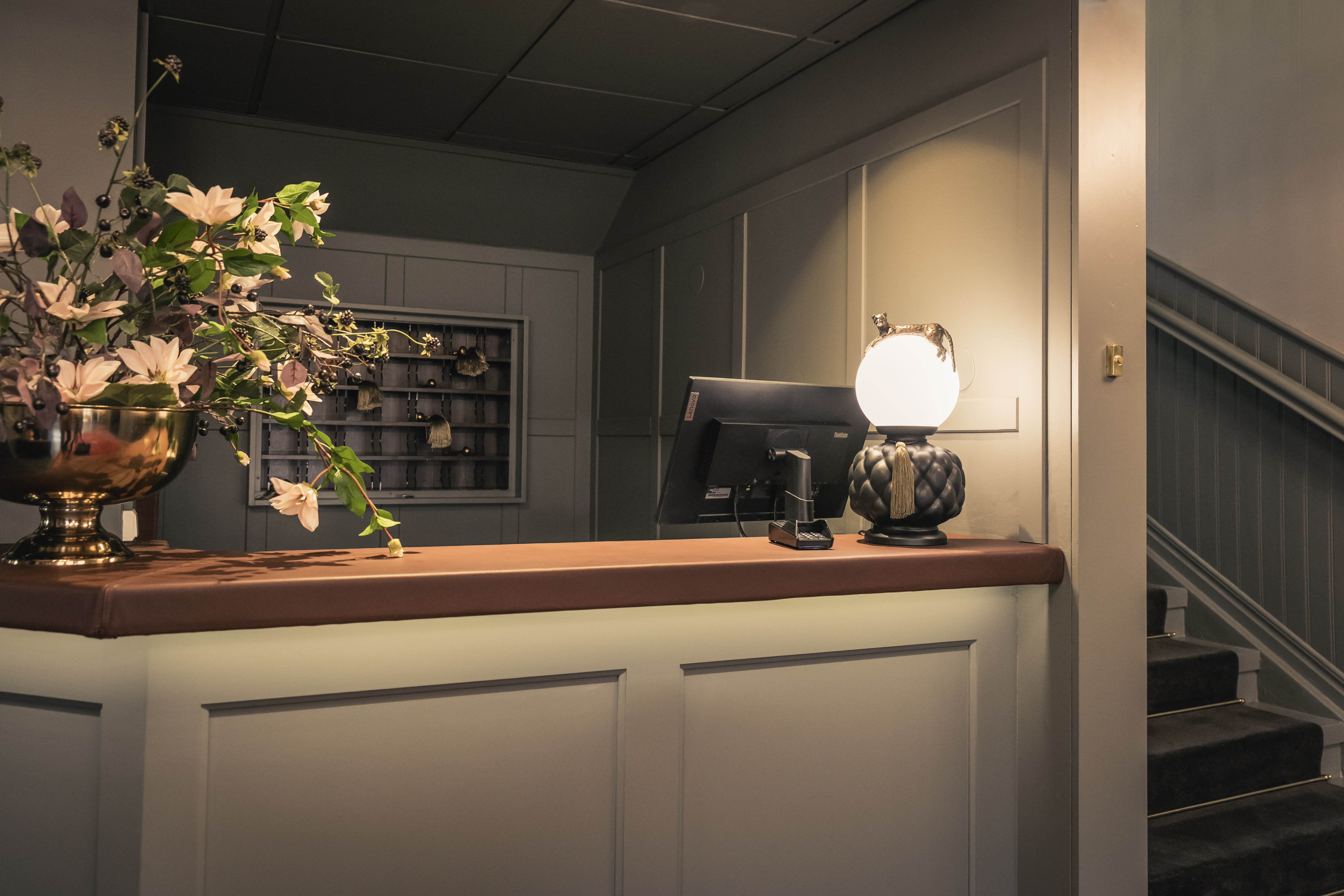 En receptionsdisk i grått med ett blomsterarrangemang och en bordslampa.