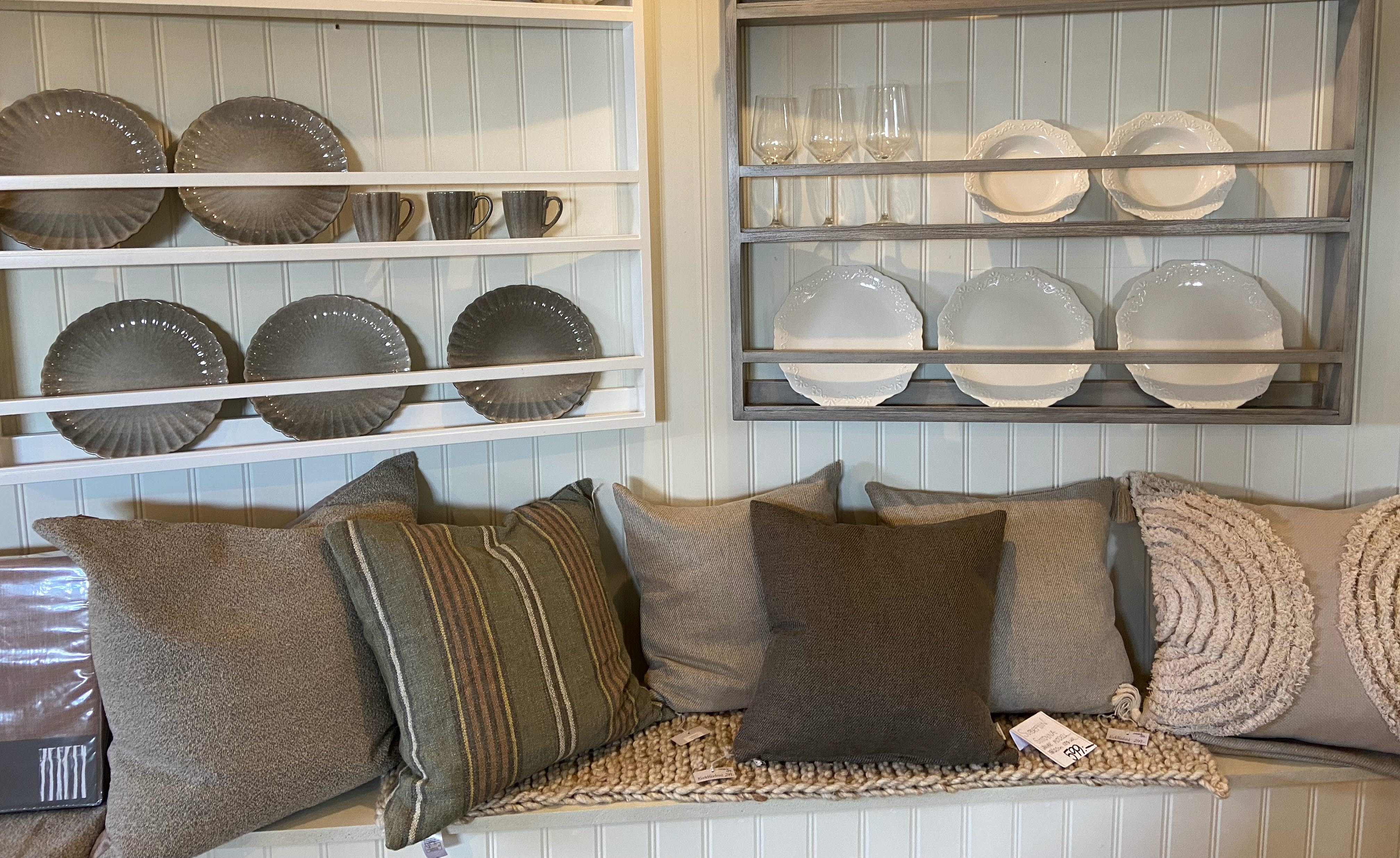 En bänk med kuddar i bruna färger. Ovanför sitter en hylla med tallrikar.