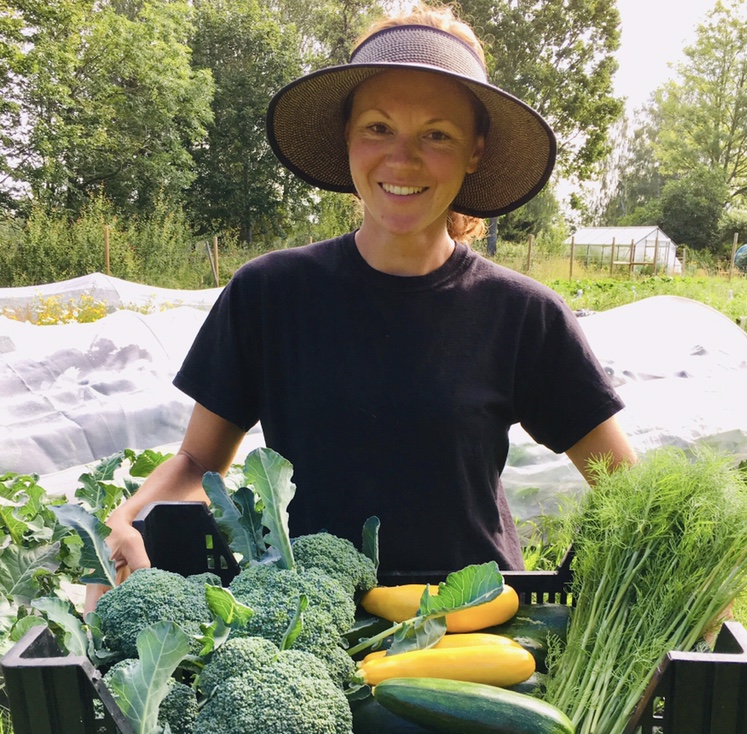 en kvinna som håller en låda med grönsaker