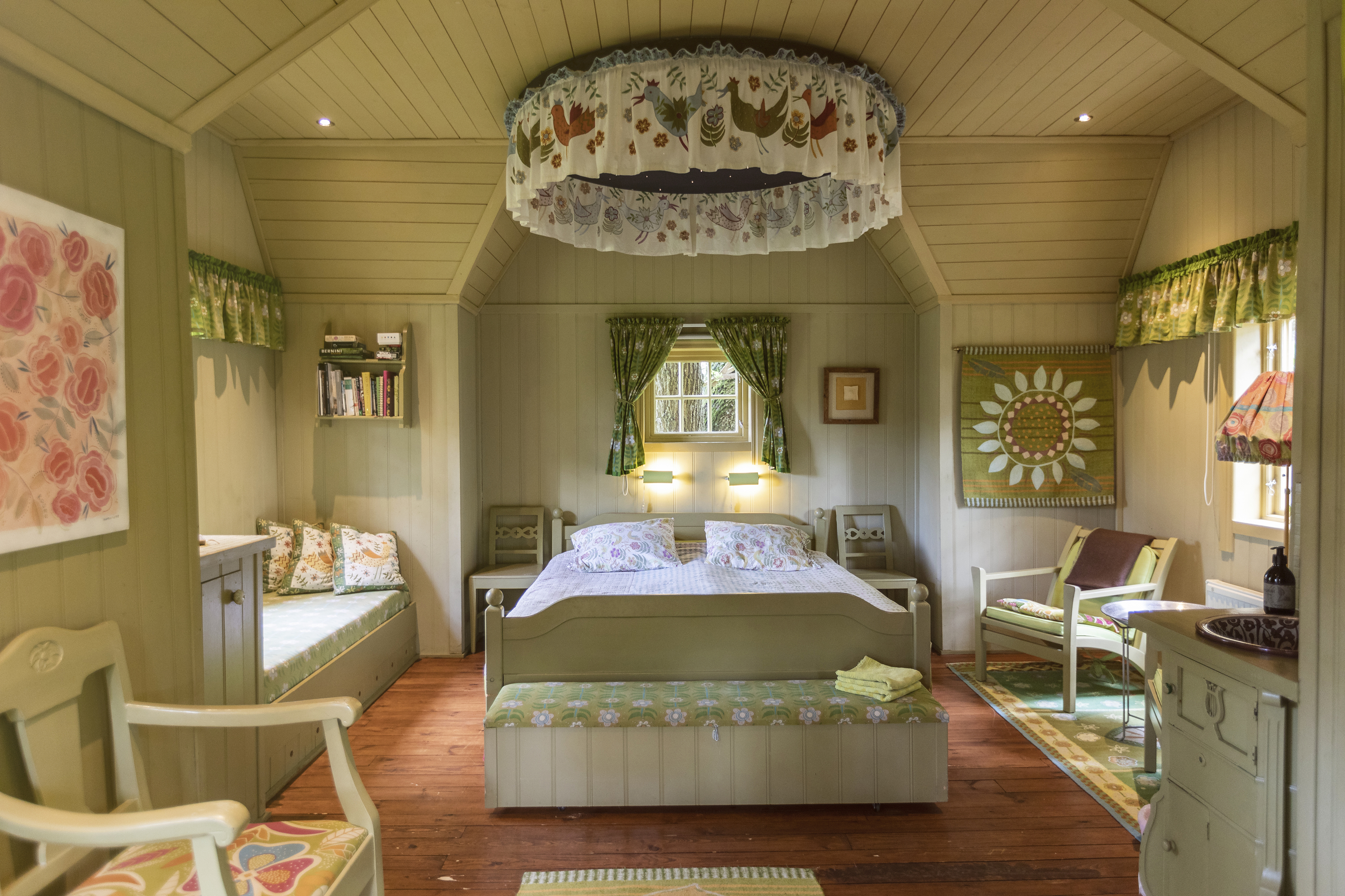 Rum med inredning i gröna toner. Träväggar, en stor dubbelsäng och sänghimmel.