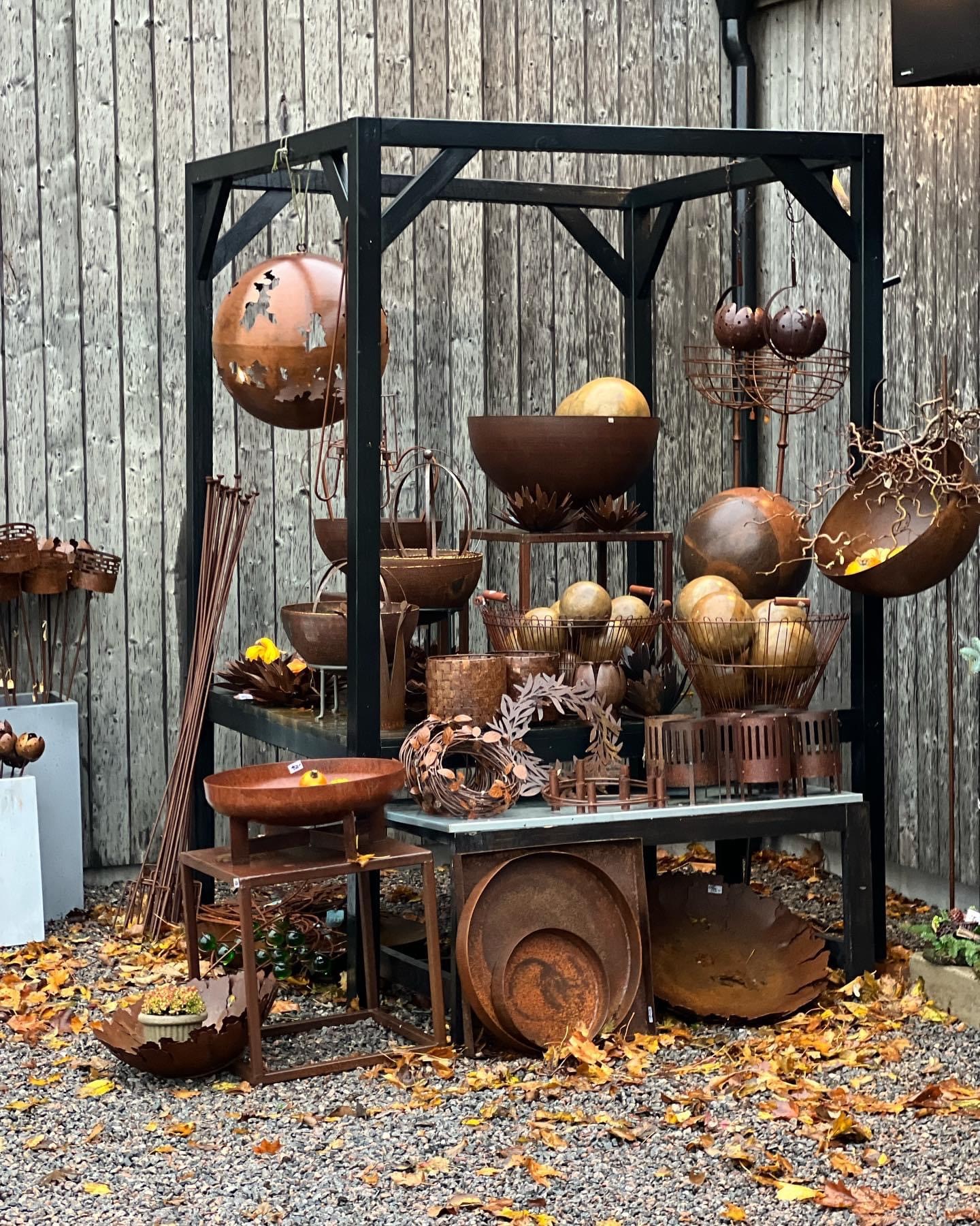 En svart ram i trä med en stor hylla där krukor och lyktor i rostat material står.