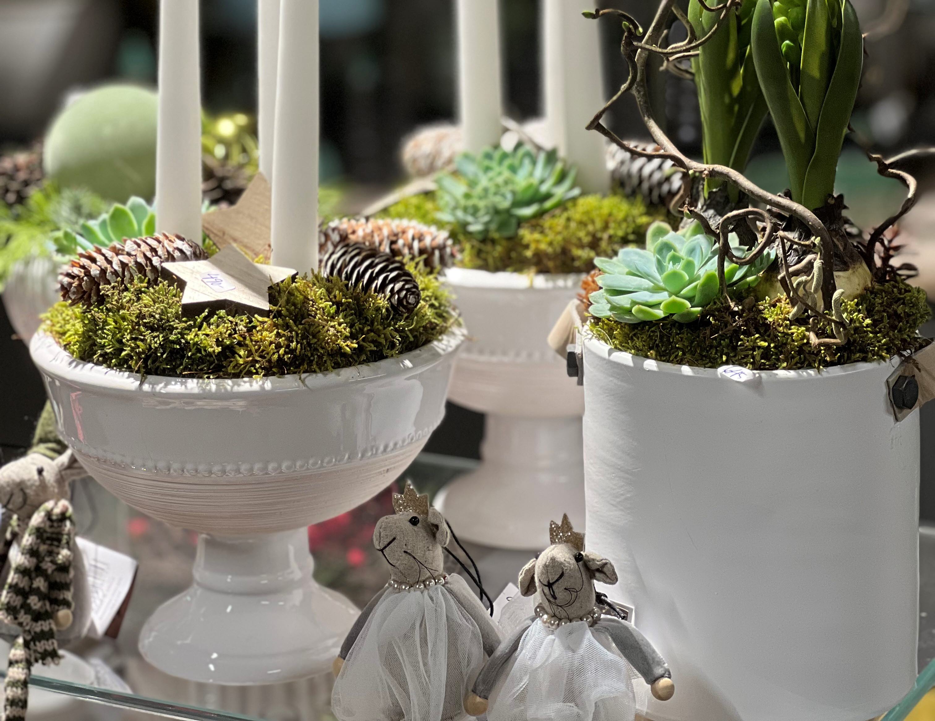 Vita krukor med juldekorationer med mossa, blommor och ljus.