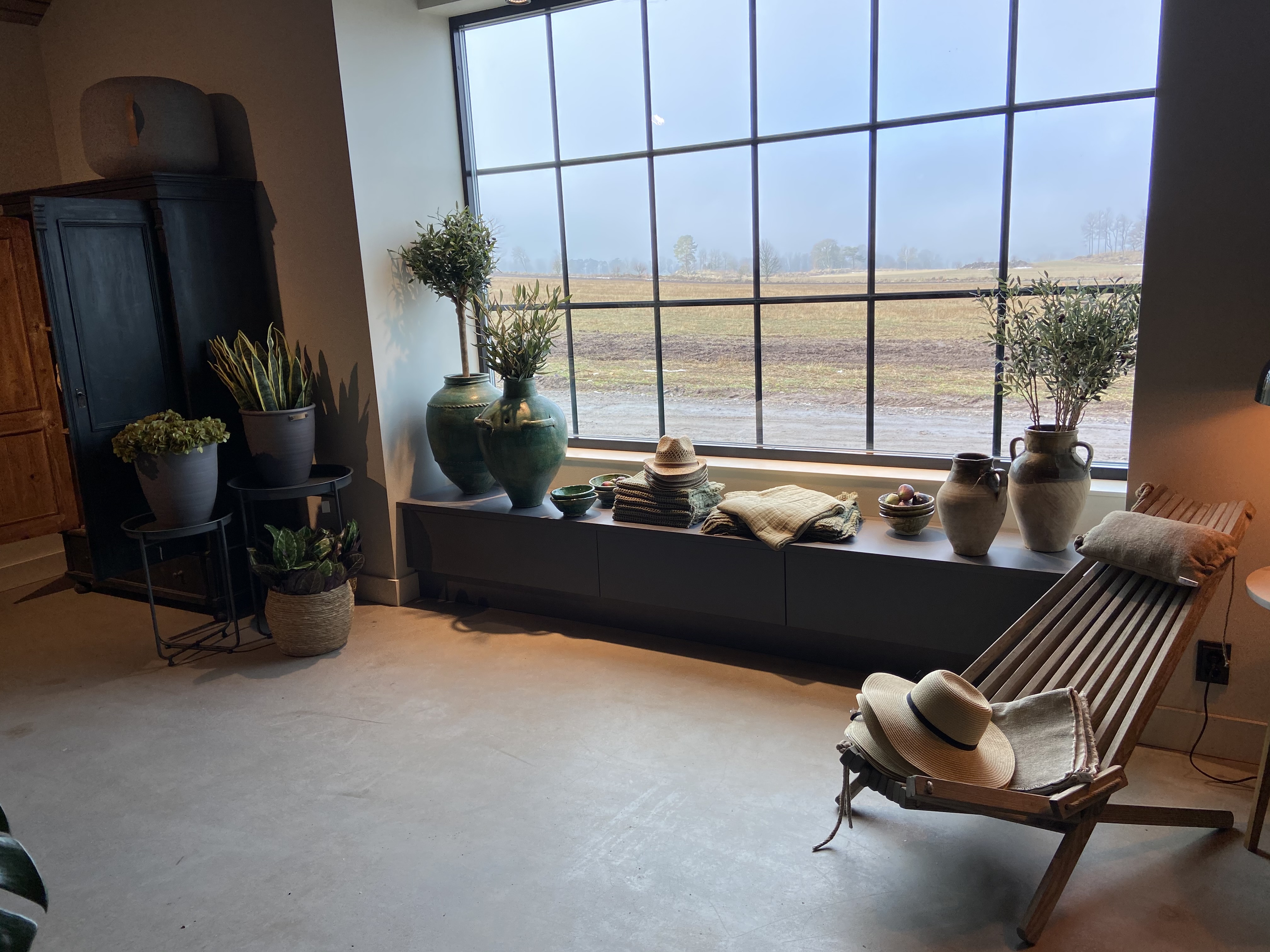 Large window with plants and a wooden deck chair.