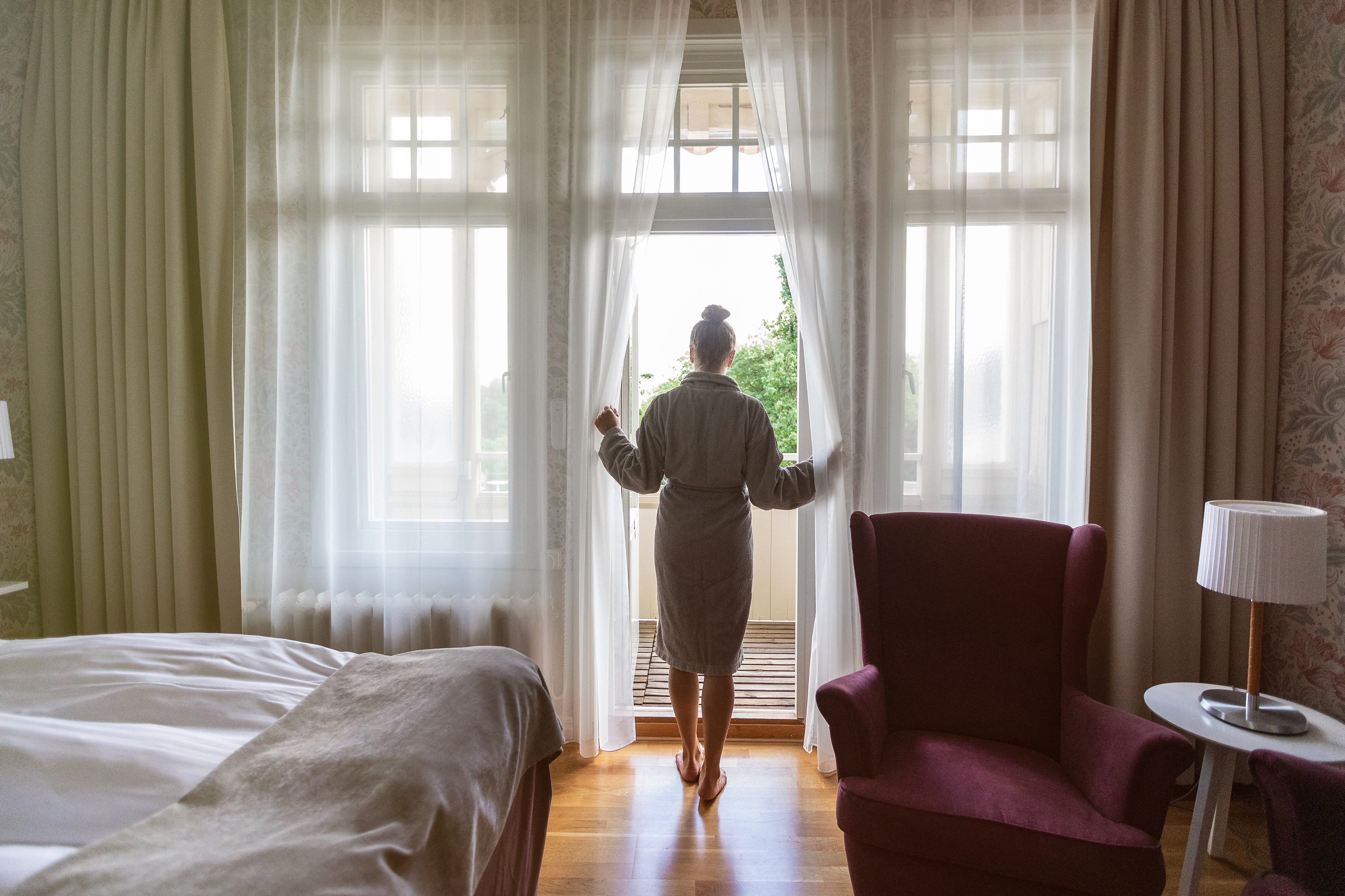 Kvinna i morgonrock står i dörröppningen till balkongen på hotellrummet.