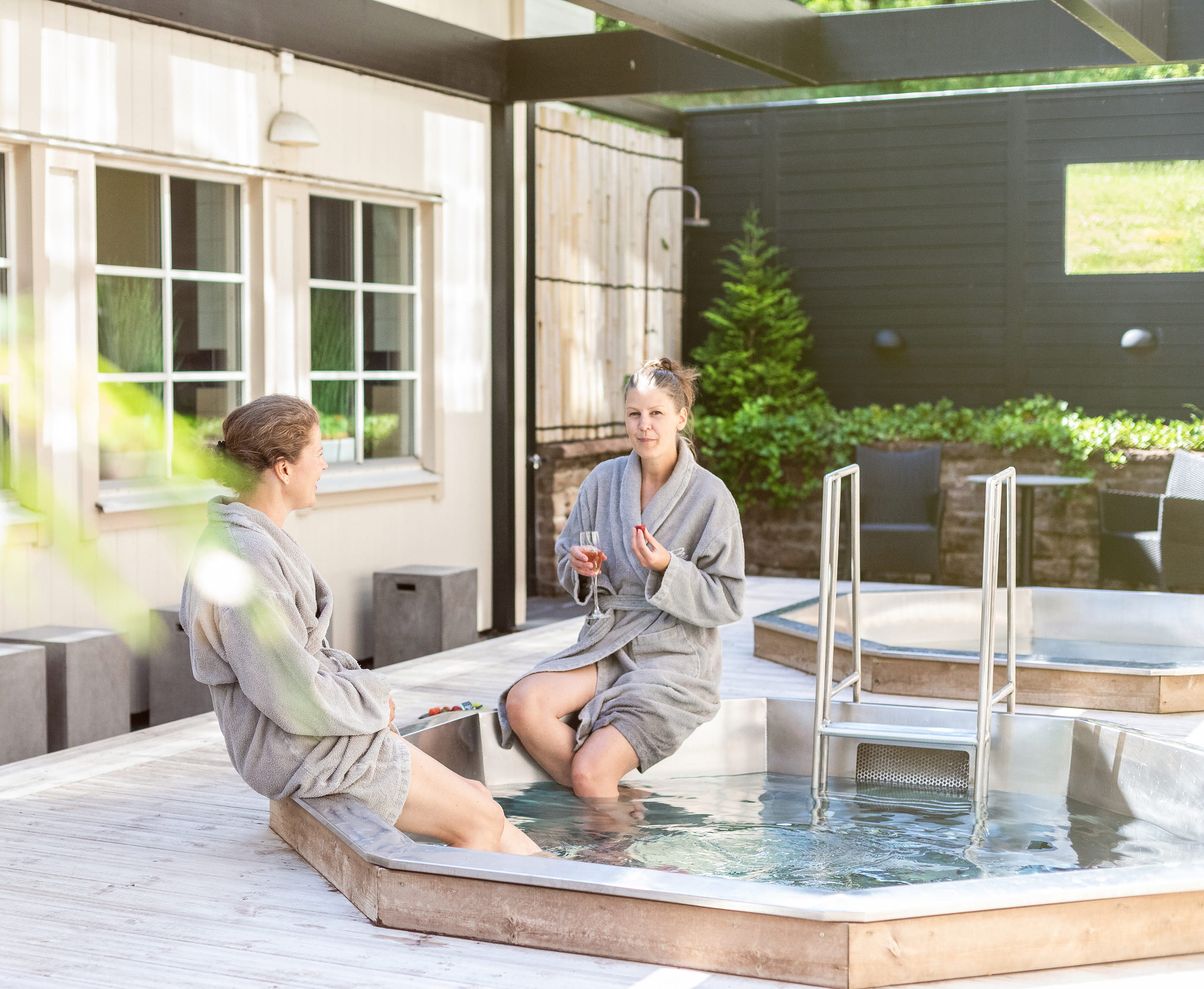 Two women sitting with bathrobes by an outdoor pool.
