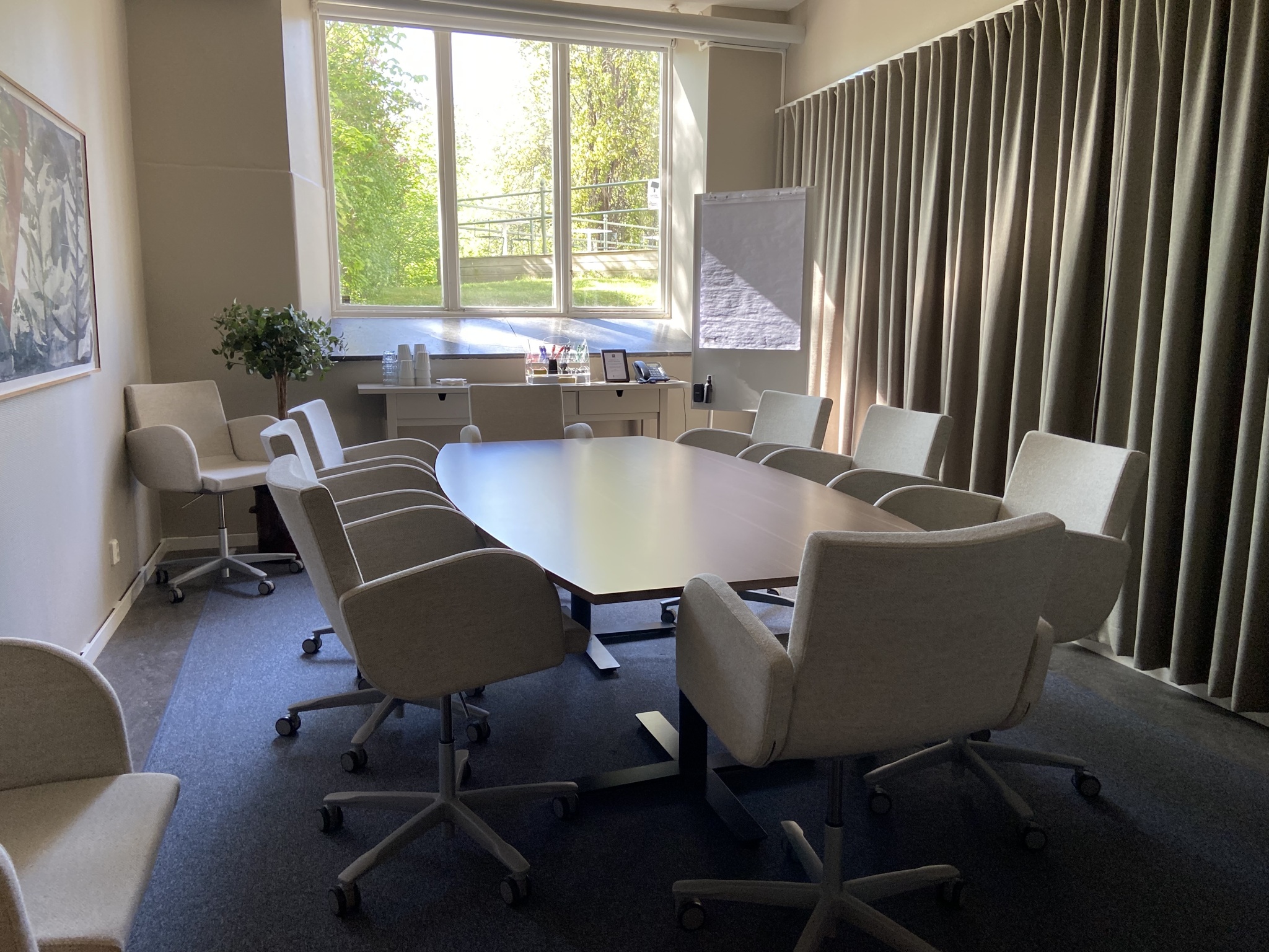 Konferensbord med stolar, ett fönster med grönska utanför.