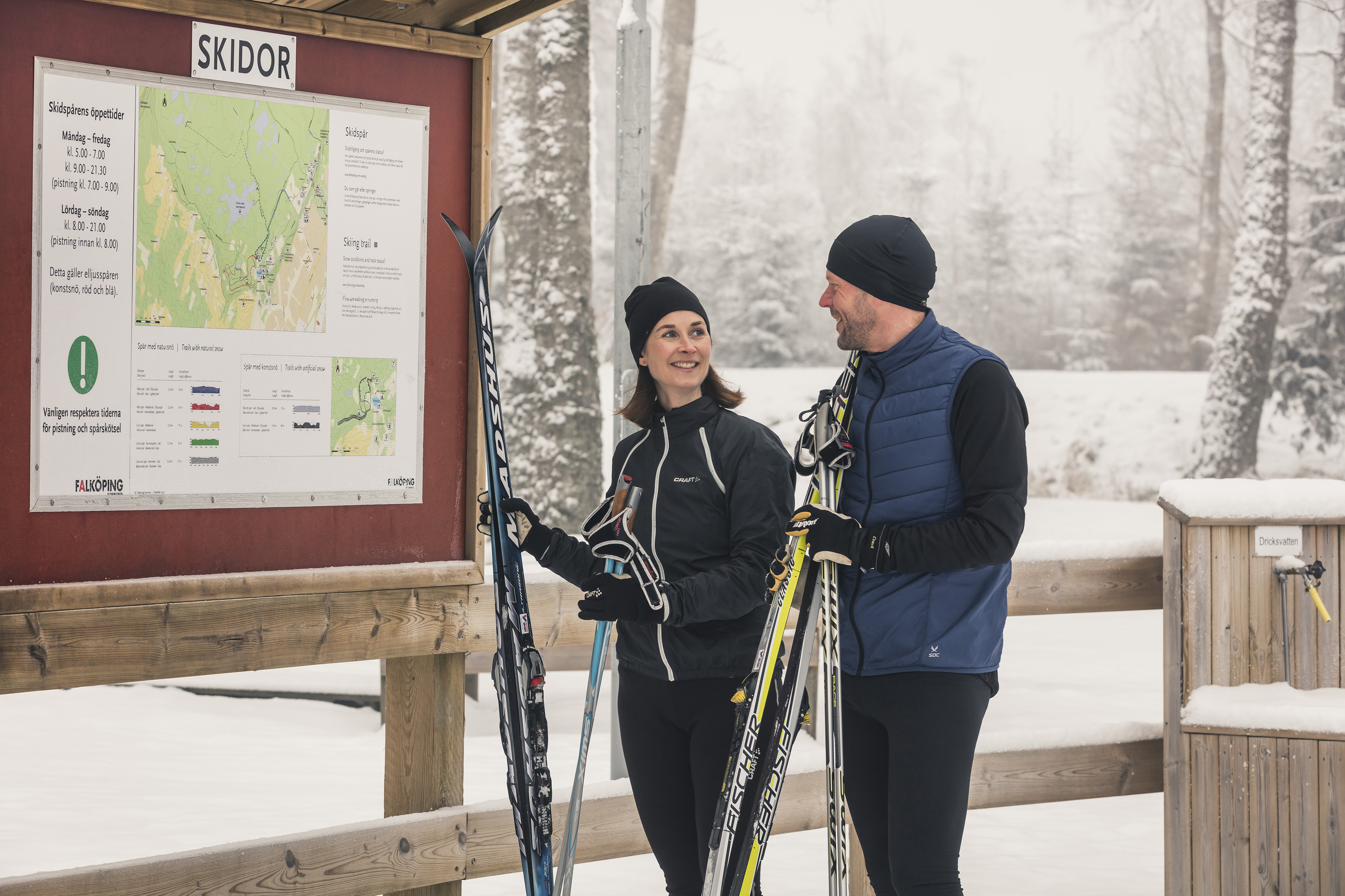 Man och kvinna som står framför en översiktskarta för skidor. De håller i sina längdskidor. 