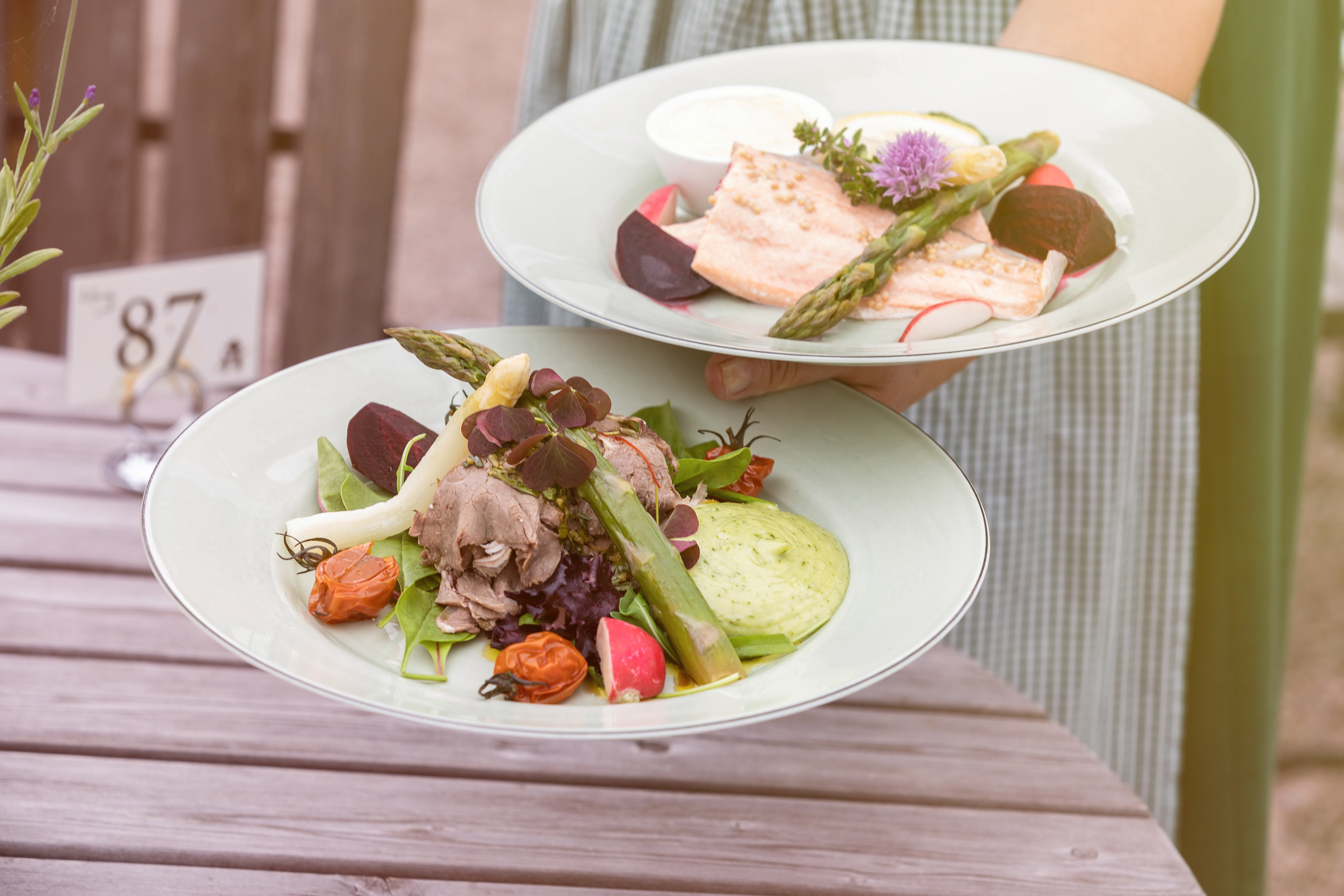 A person holding up two plates of food. One with meat and vegetables one with salmon.