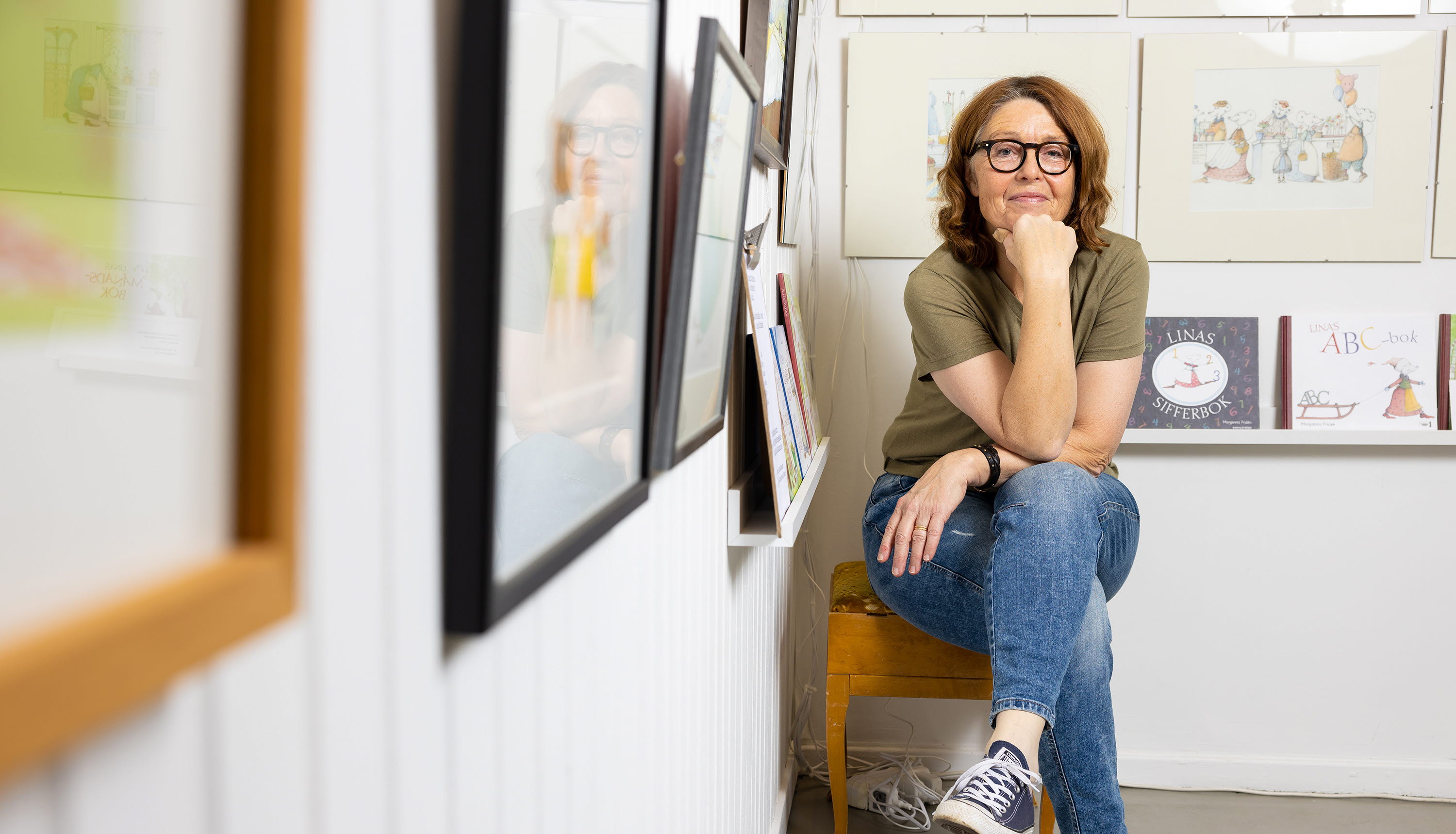 En kvinna sitter på en pall i ett galleri med tavlor på väggarna.