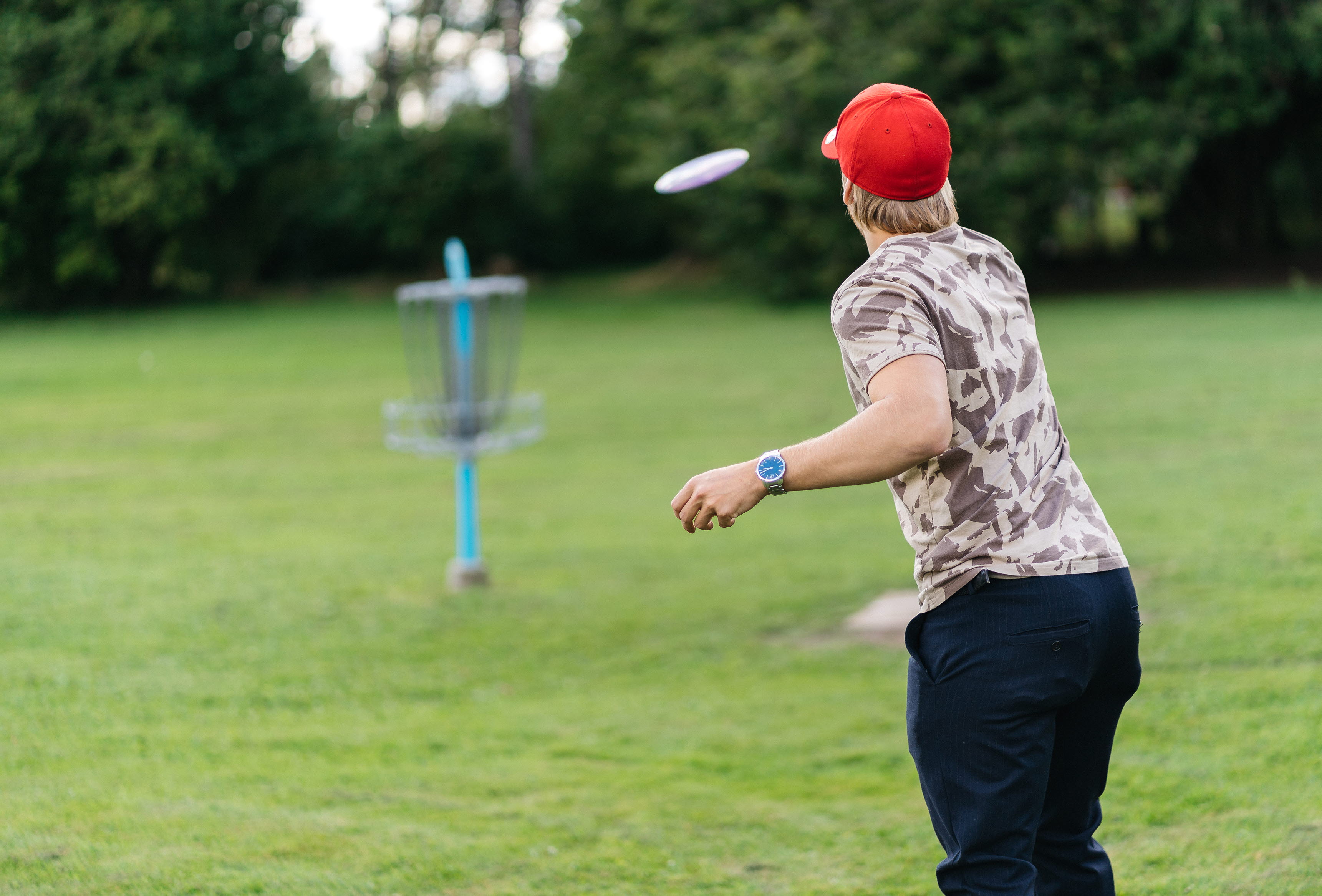 Kille med röd keps som kastar en frisbee mot en korg.