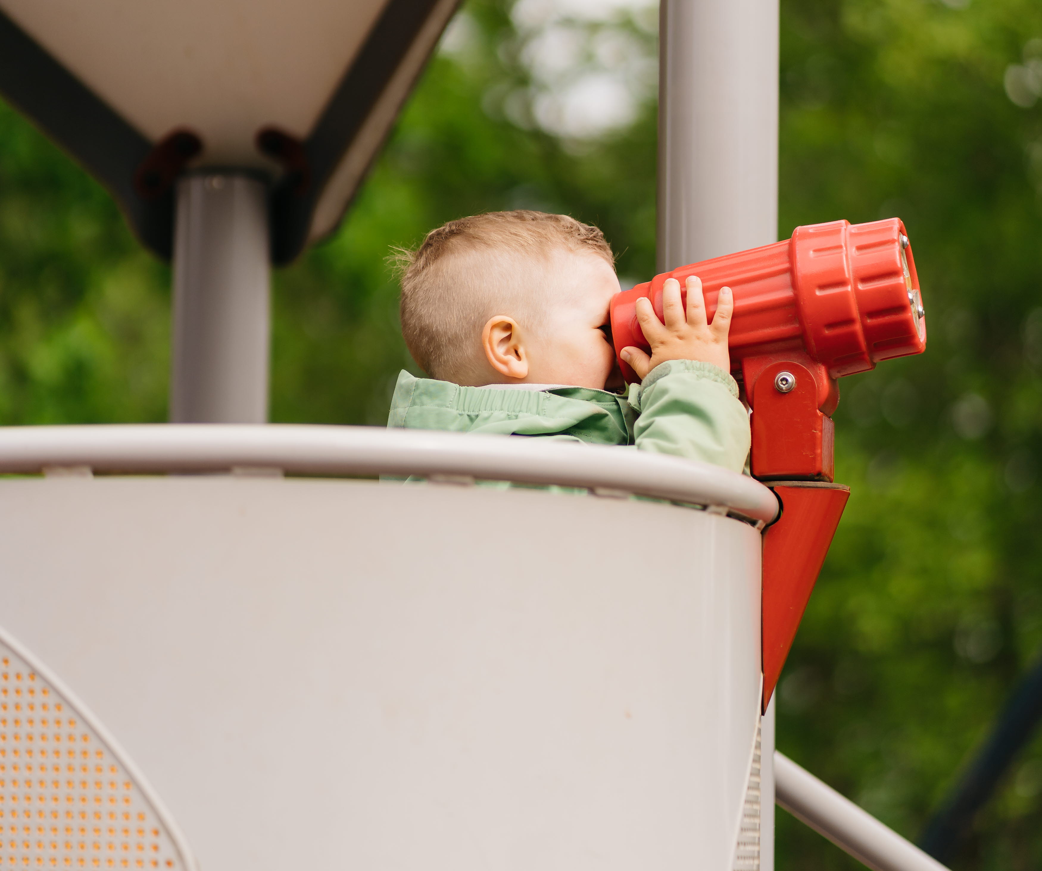 Pojke som står i en klätterställning och kikar i en röd plastkikare.