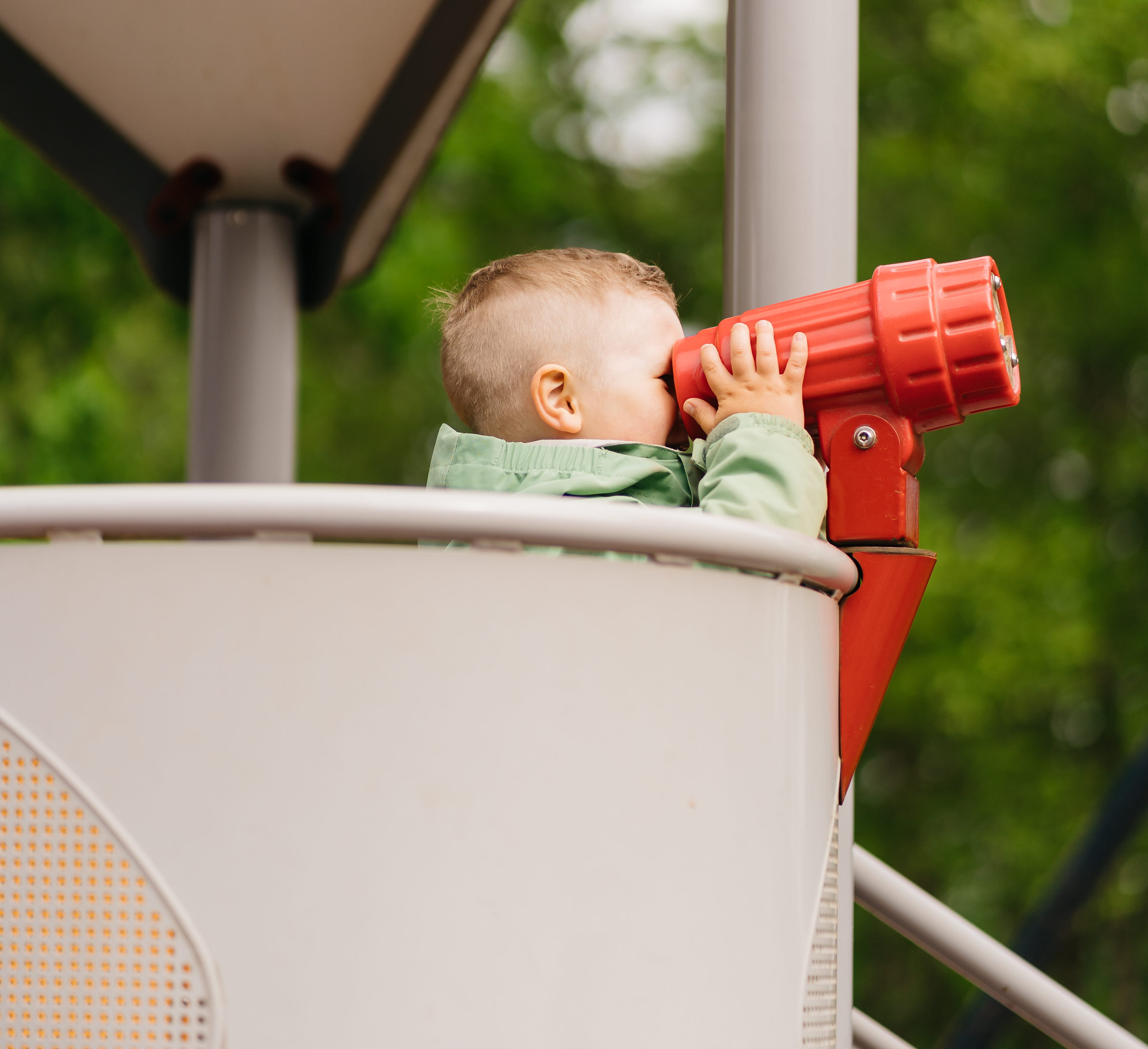 Pojke som står i en klätterställning och kikar i en röd plastkikare.