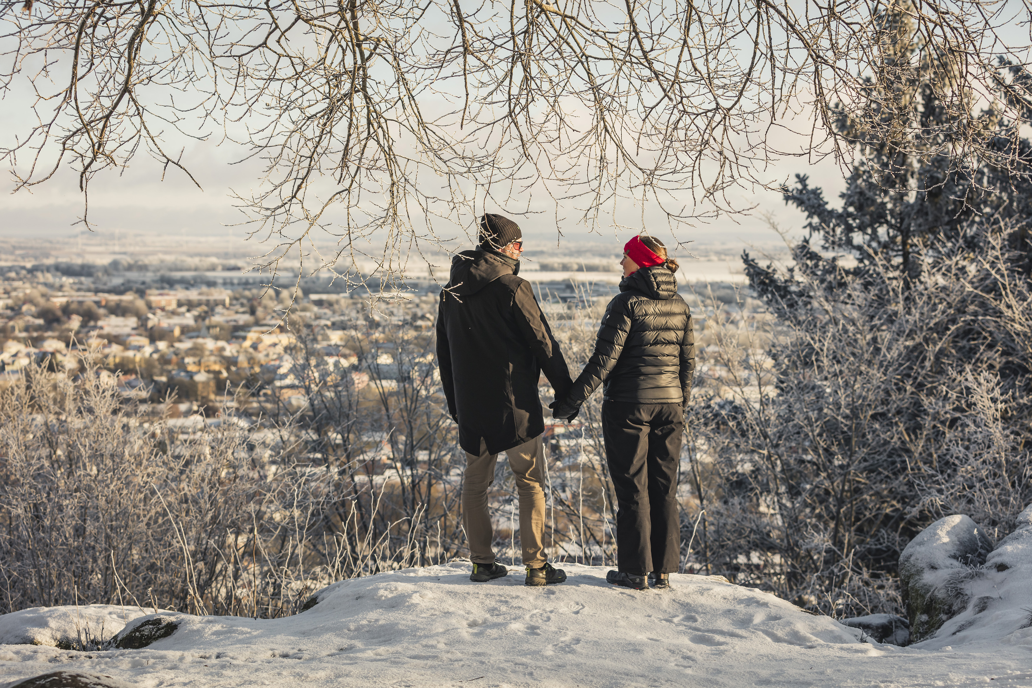 Man and woman in winter clothes peeking at the view of the city. Snowy and frosty landscape